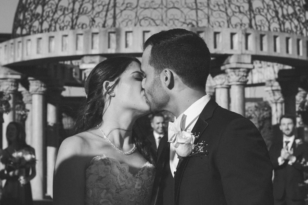 Romantic wedding ceremony kiss under classical architecture and columns.