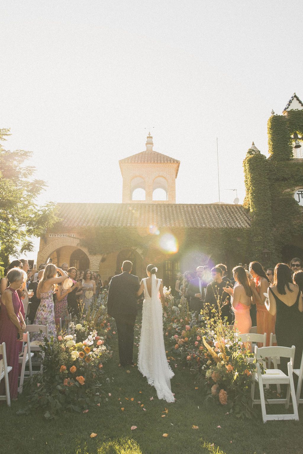 Outdoor wedding ceremony at sunset with guests and floral decorations.