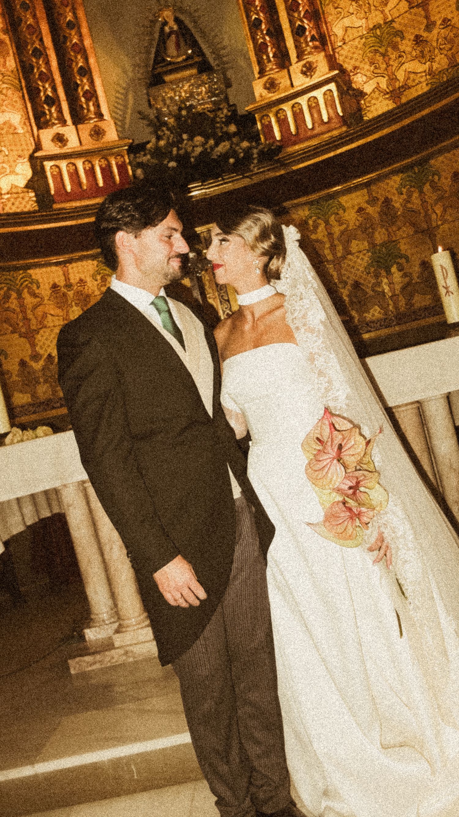 A wedding couple in formal attire standing in an ornately decorated venue with golden walls.