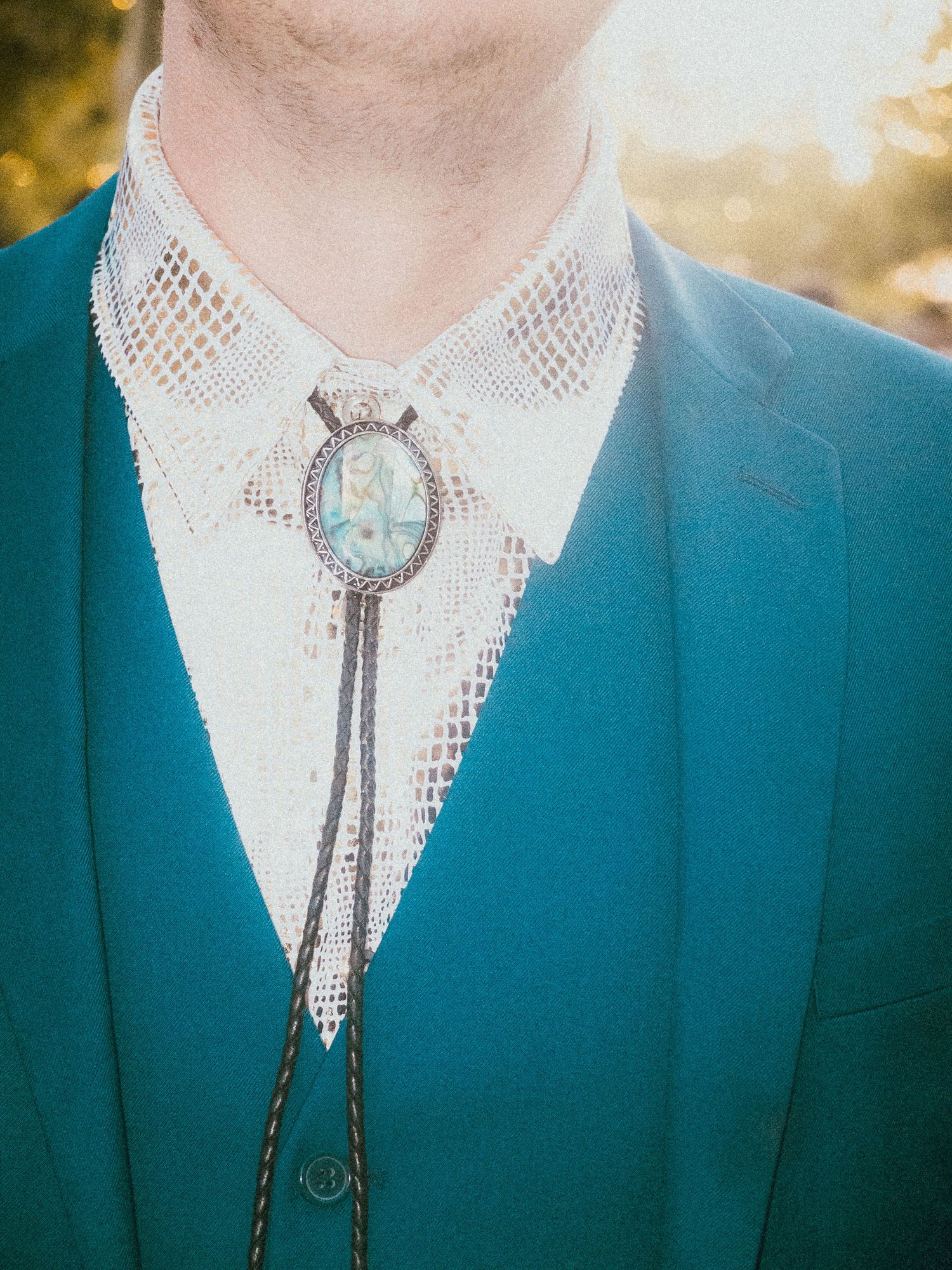 Close-up of a turquoise bolo tie with silver details on a white collar.