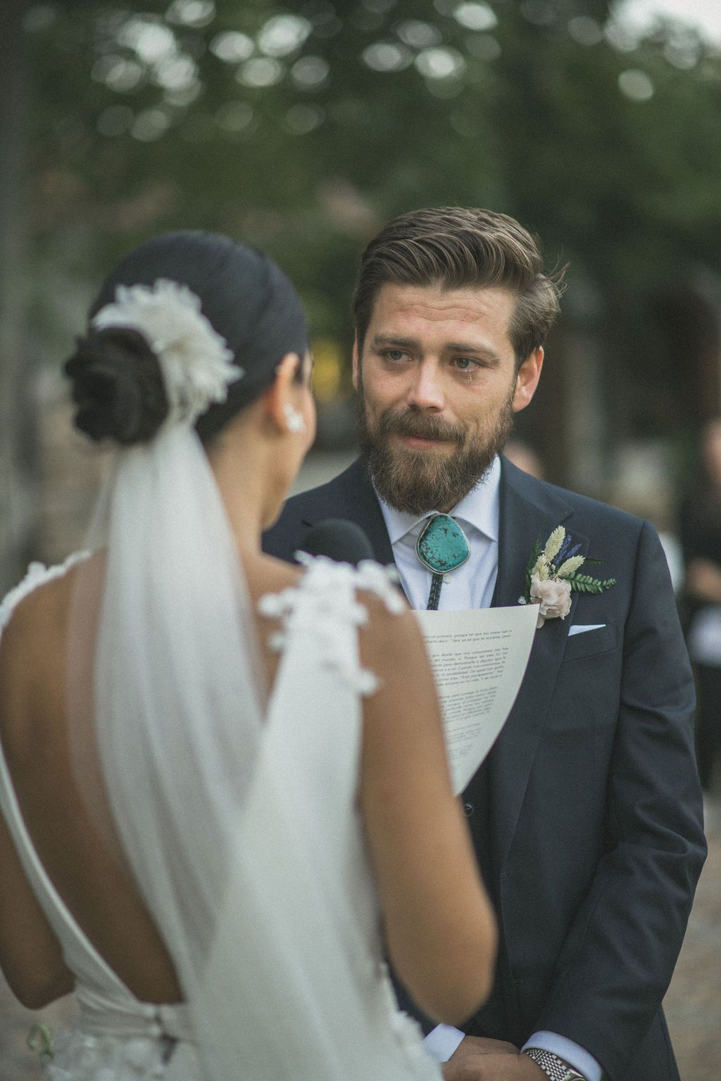 Intimate wedding ceremony moment showing a couple exchanging vows outdoors with pink flowers in background.