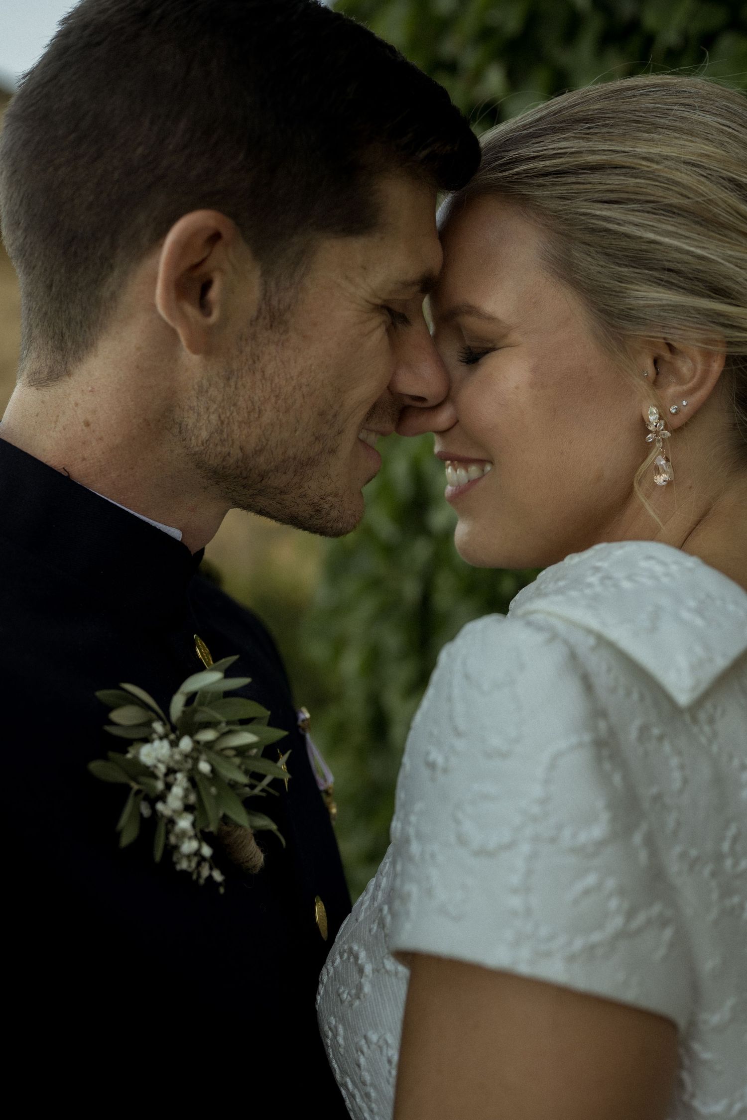 Intimate wedding portrait showing a tender moment between newlyweds with the bride in lace and groom wearing a floral boutonniere.