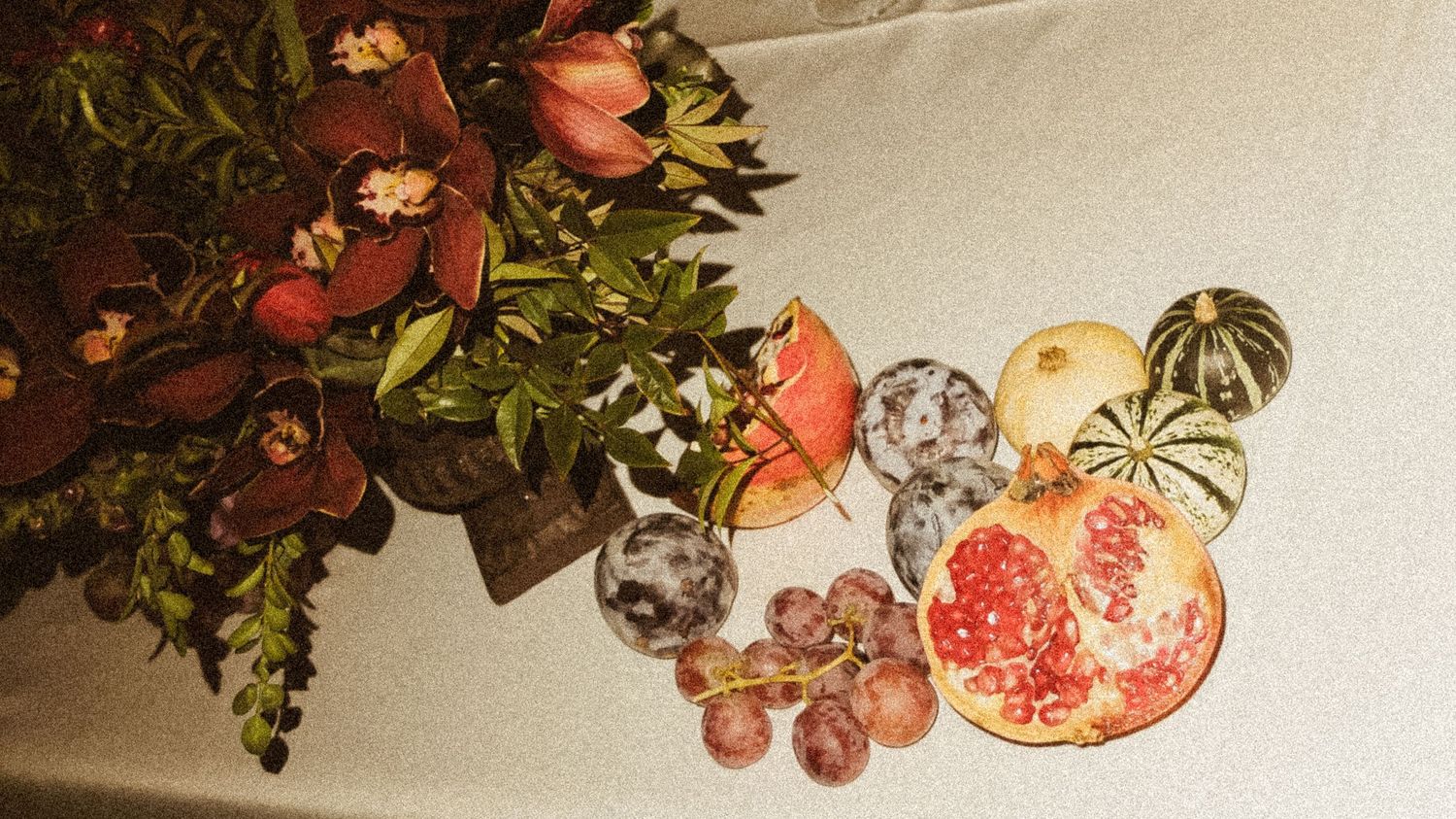 Decorative fruit and floral arrangement with pomegranates and roses on a light background.