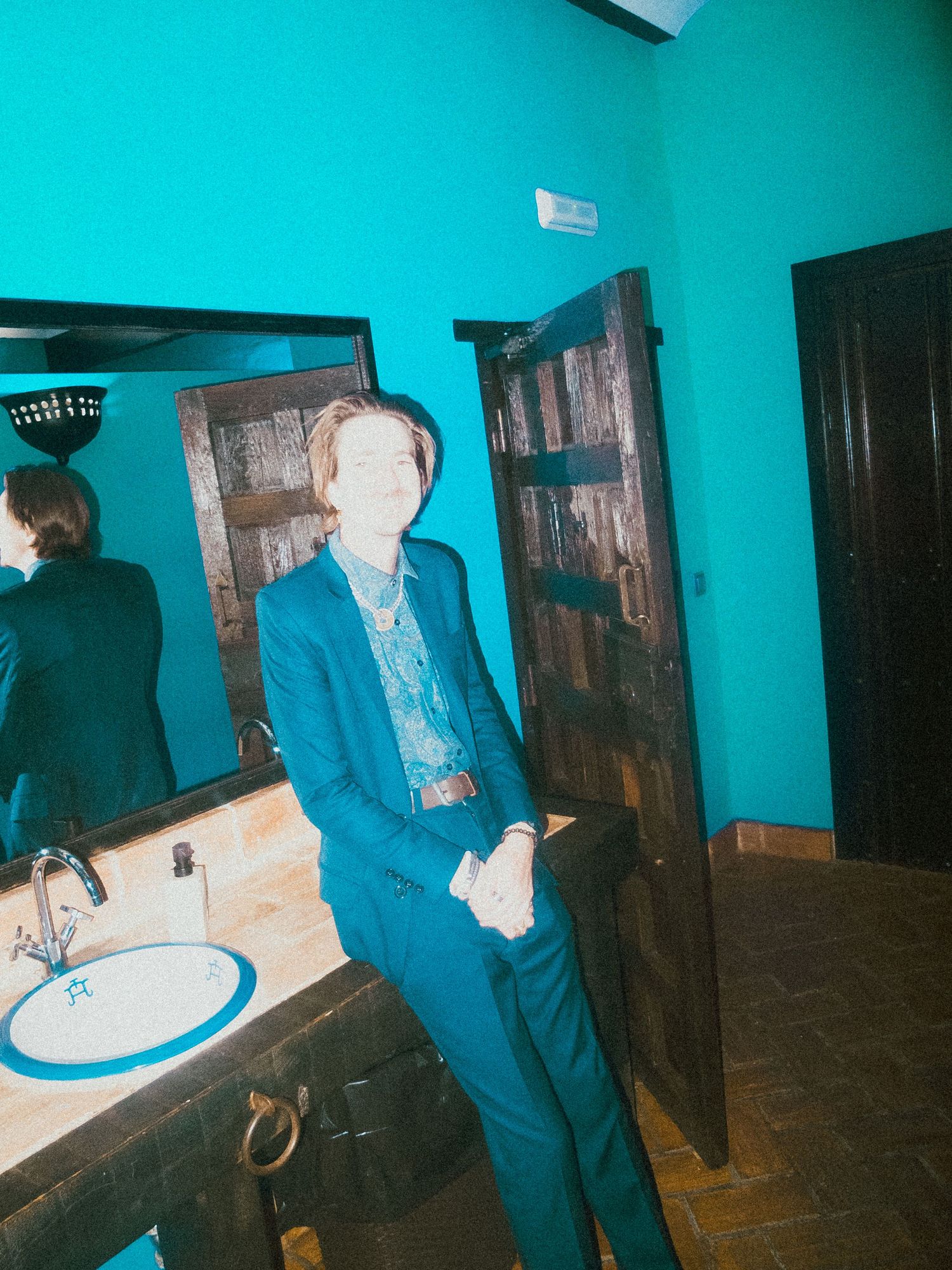 People in formal attire standing in a hallway with bright turquoise walls.