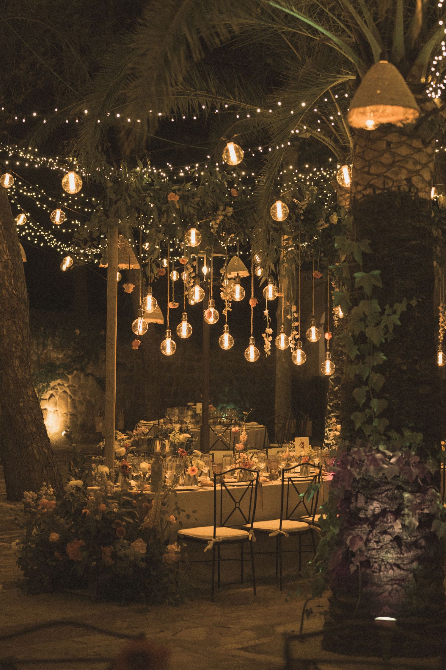 Enchanting outdoor dining area decorated with hanging string lights and floral arrangements at dusk.