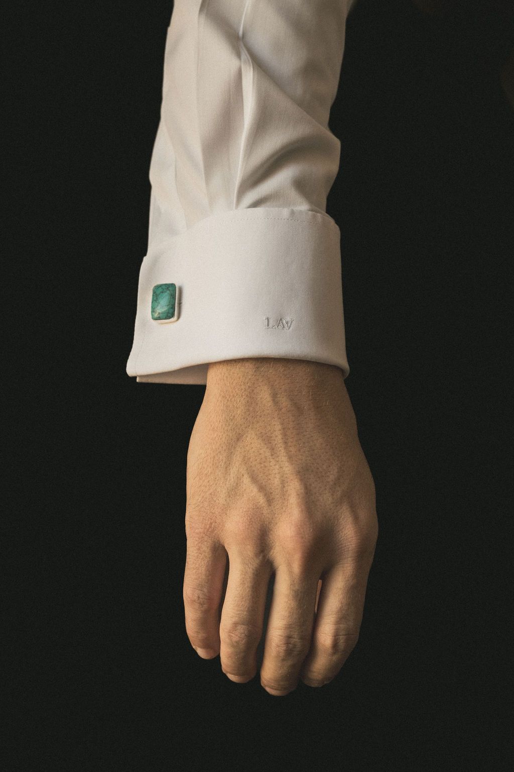 Close-up of a white dress shirt sleeve and cufflink against a dark background.