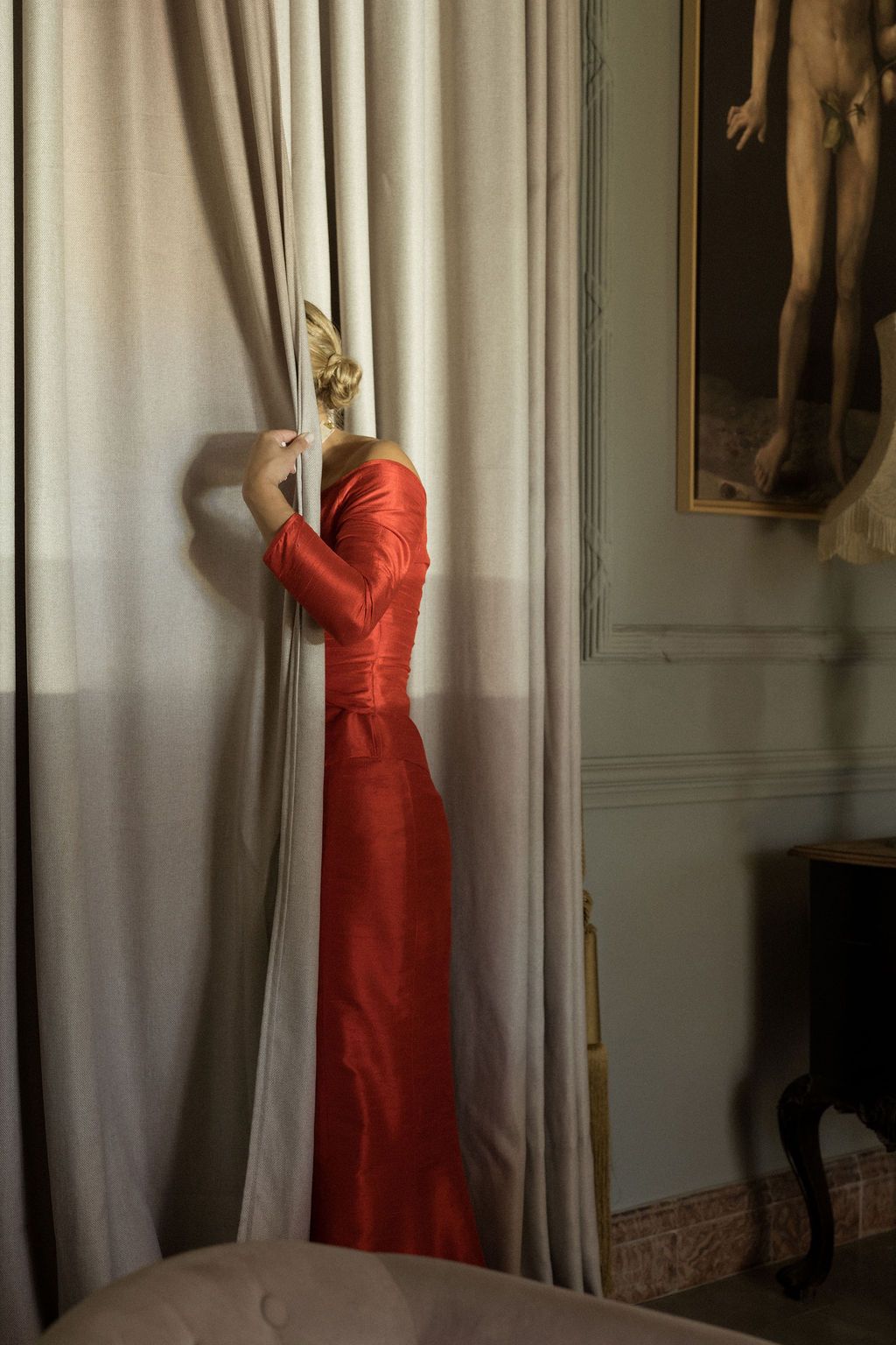 Red strapless evening gown displayed against light colored curtains in an elegant room.