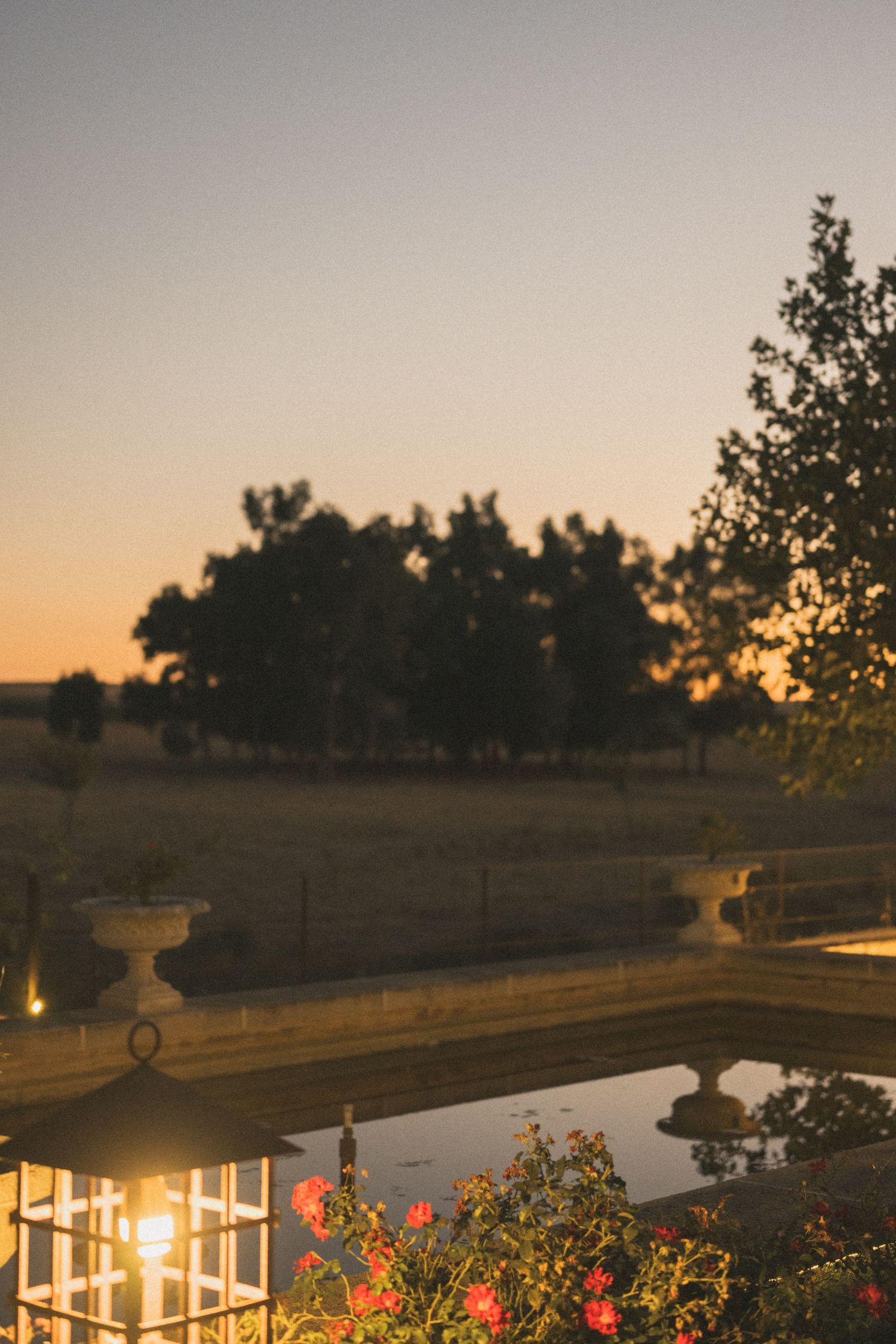 Outdoor wedding venue at sunset with string lights and floral decorations creating a romantic atmosphere.