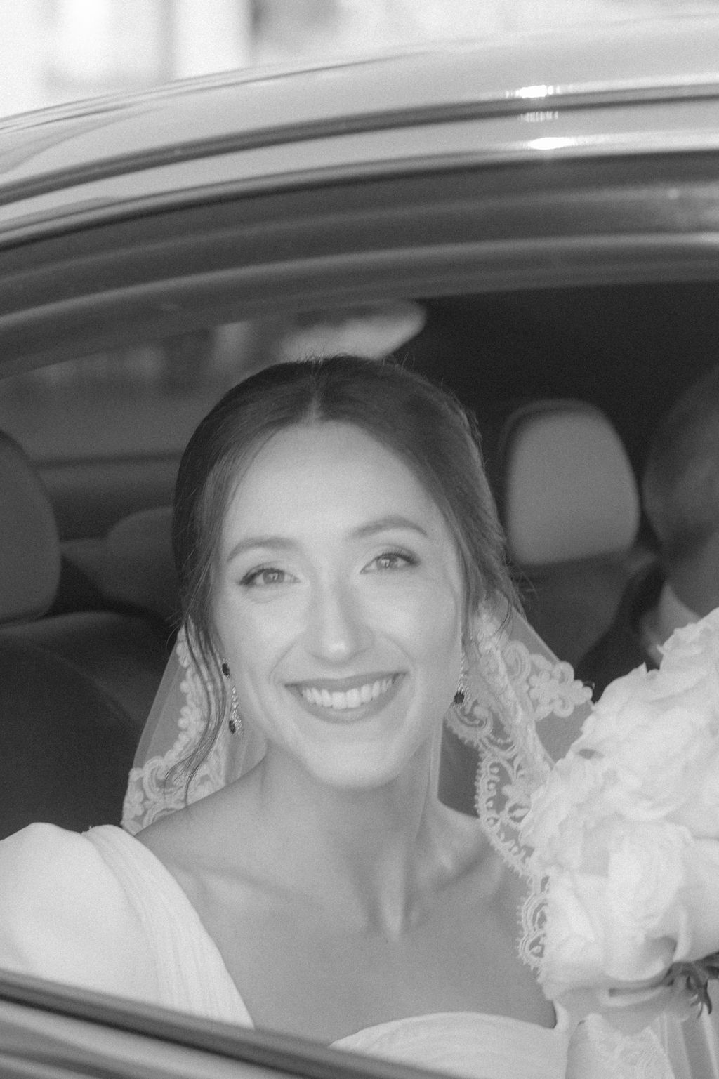 A bride smiling joyfully inside a wedding car.