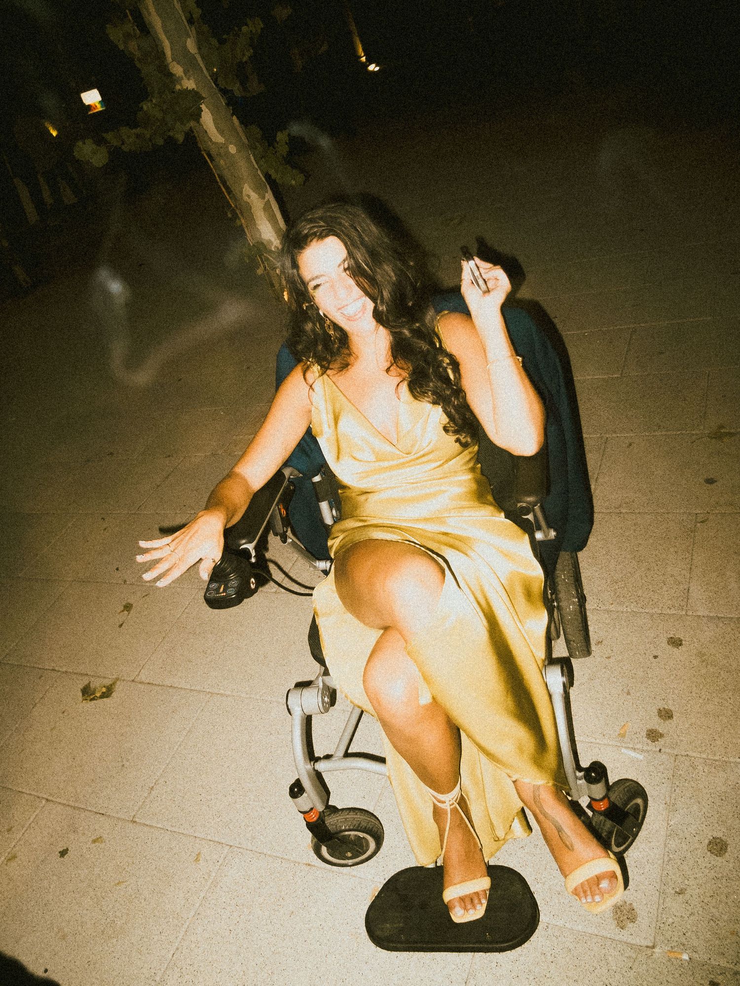 Person in a yellow dress sitting in a wheelchair at an evening event.