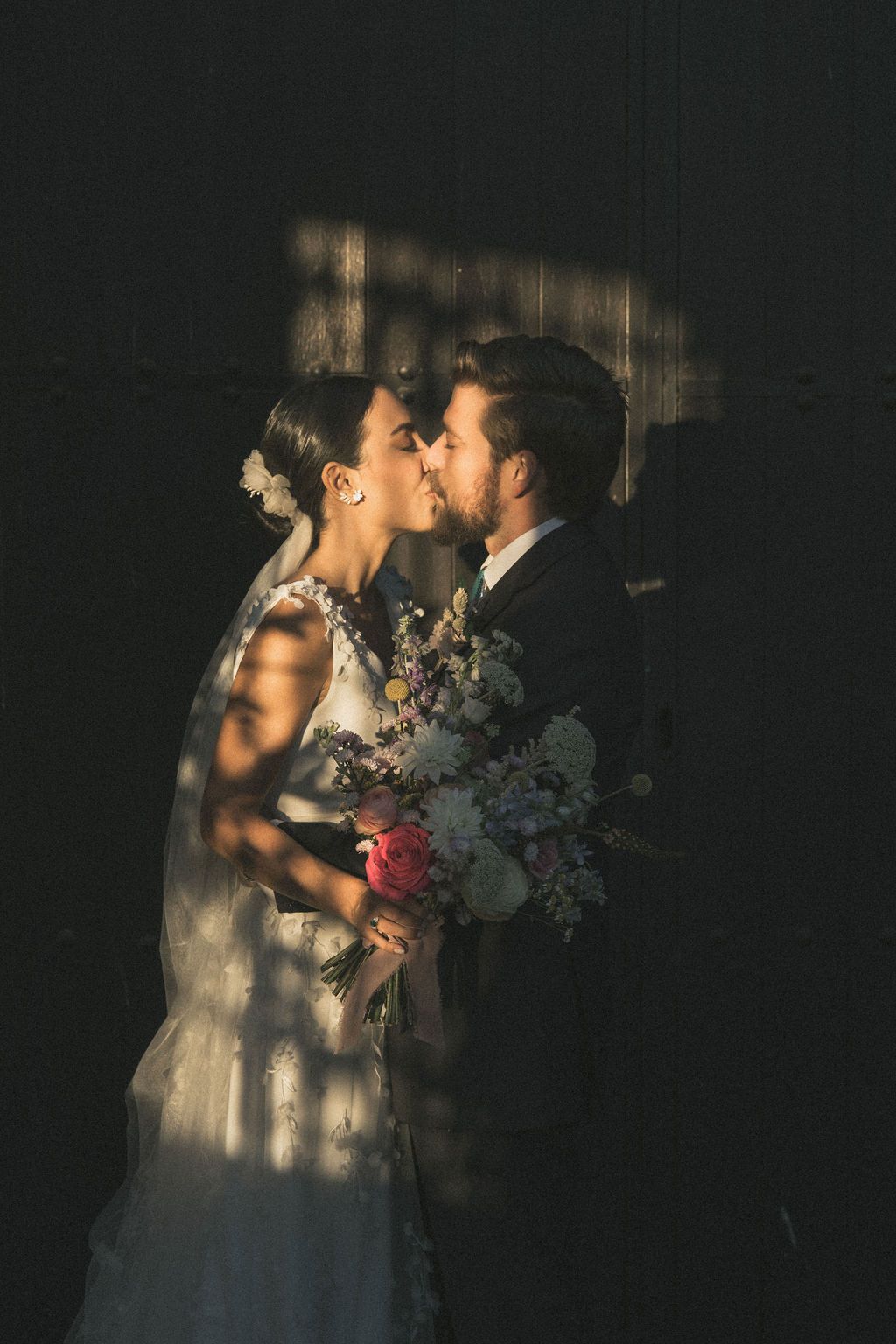 Artistic shadow play photograph of newlyweds with dramatic lighting and floral bouquet.