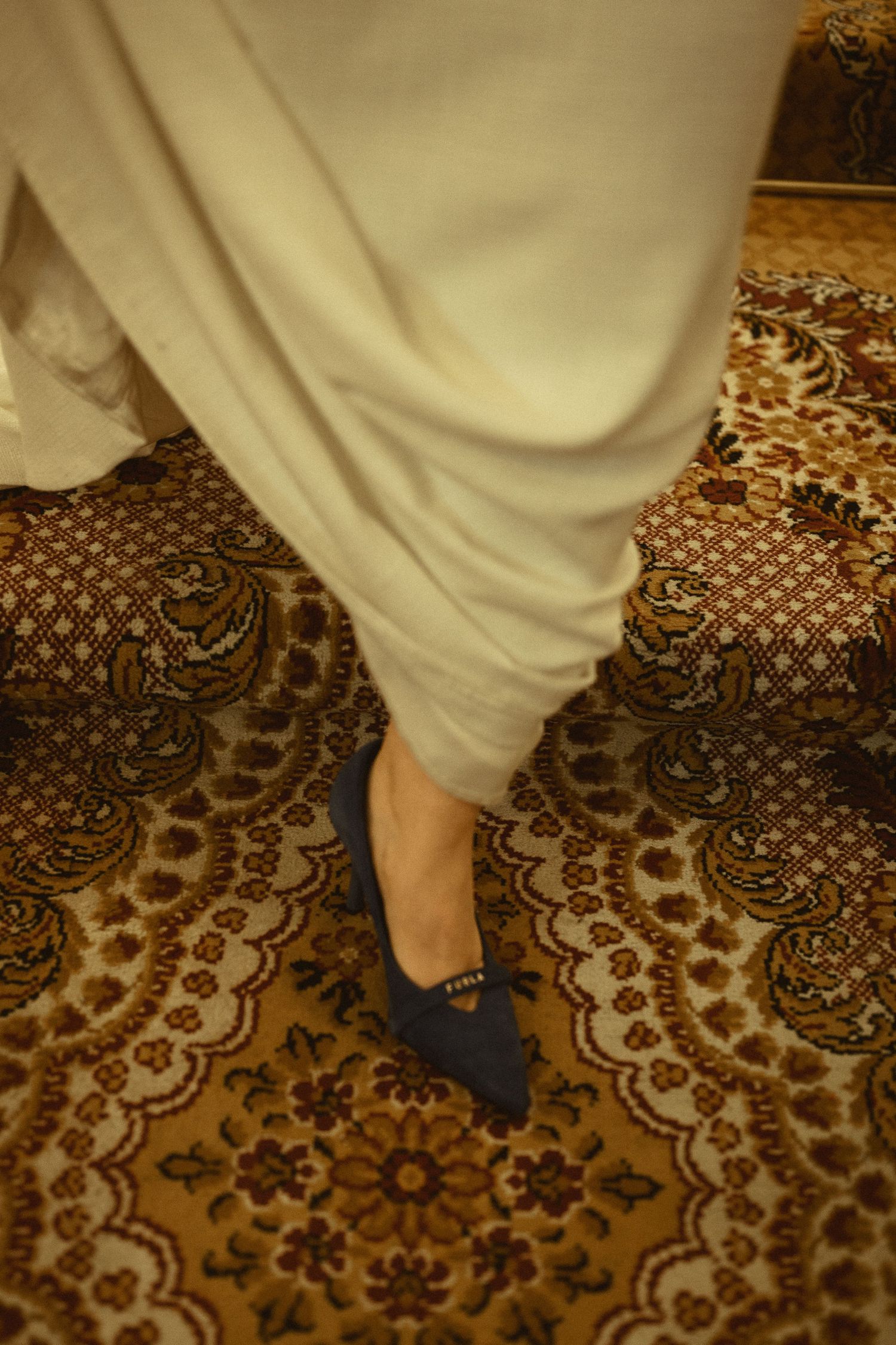 Close-up of white wedding dress hem against ornate patterned carpet.