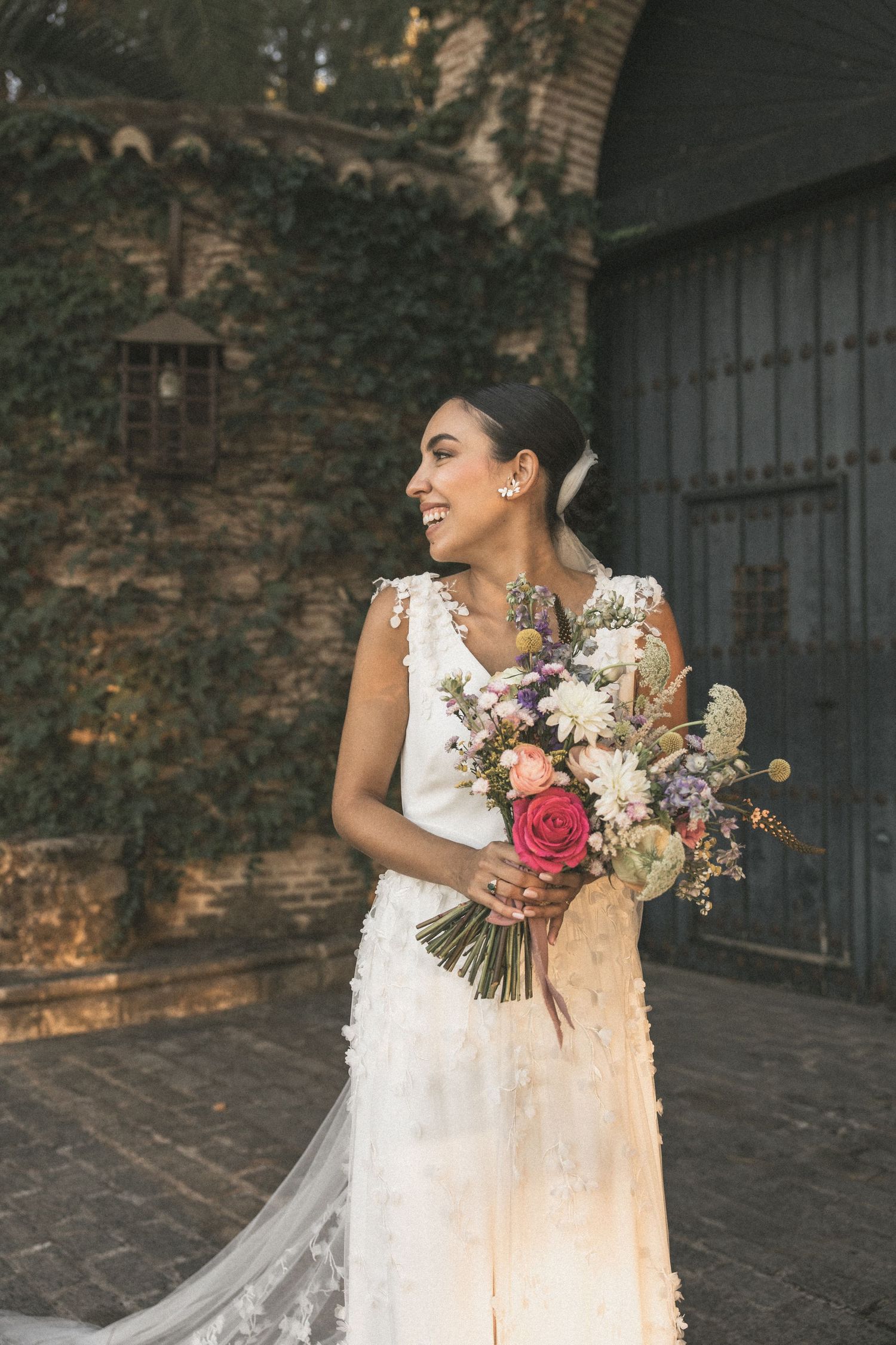 Bride holding colorful wedding bouquet against stone wall background with natural lighting.