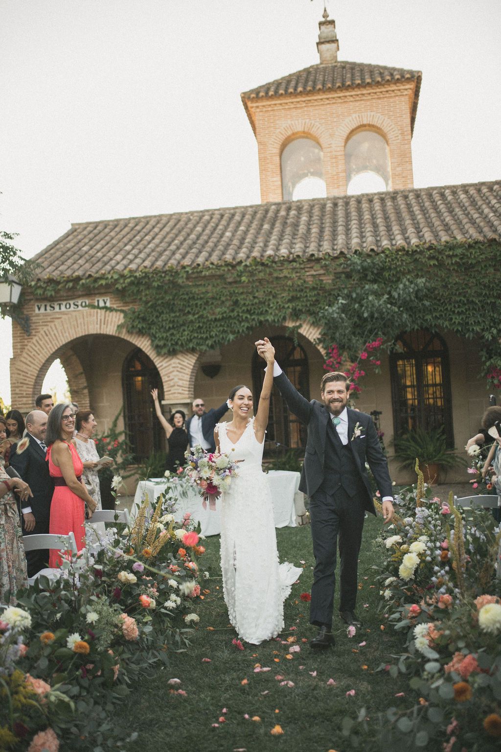 Wedding couple poses in front of Spanish-style architecture with climbing roses and ivy.