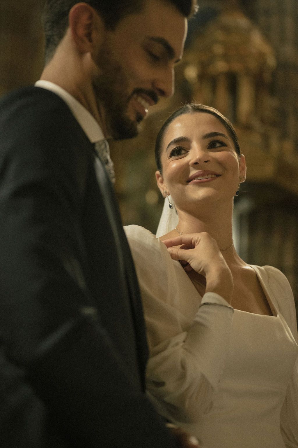 Intimate wedding moment captured in warm, dramatic lighting with elegant formal attire.