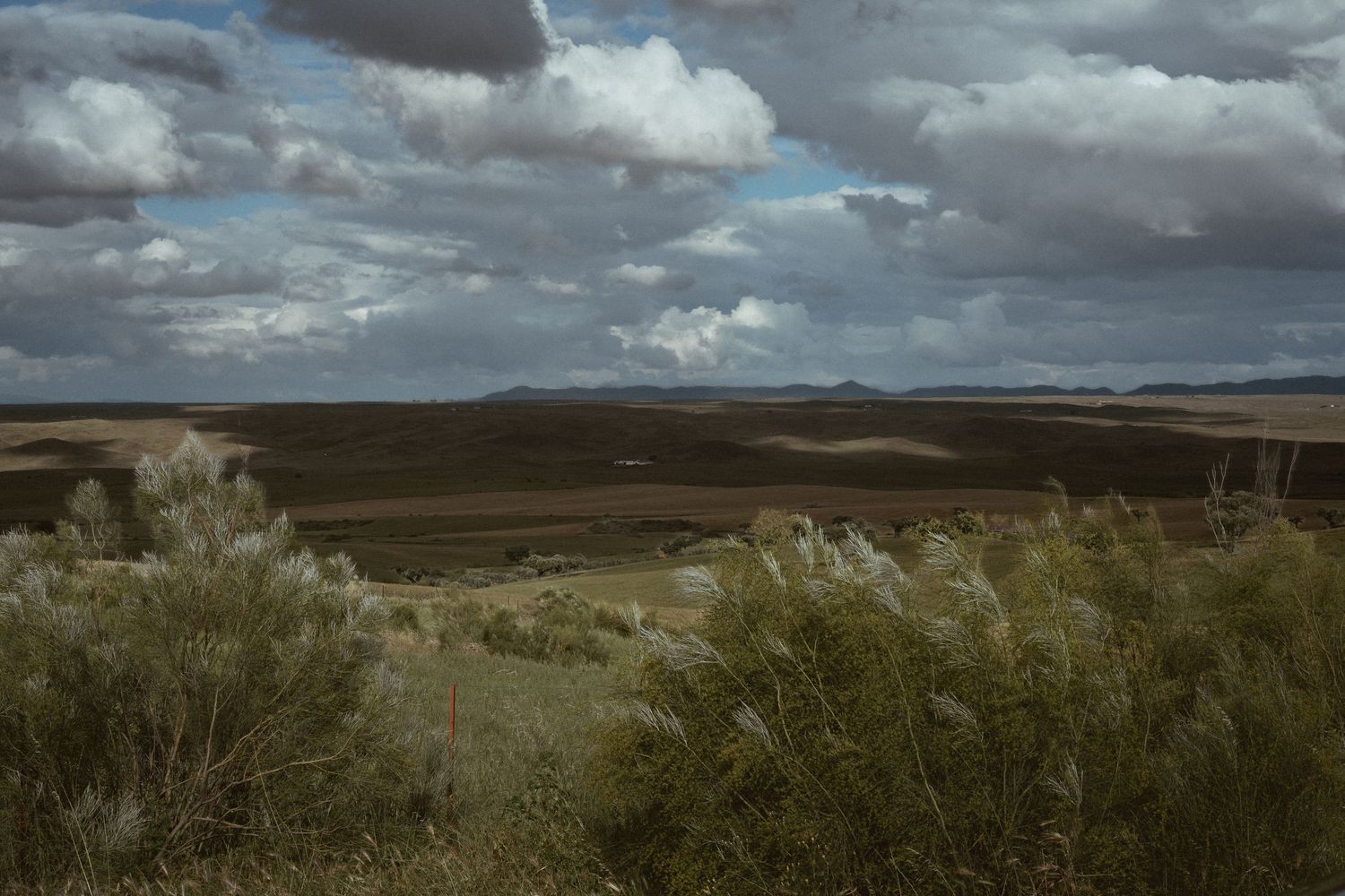 Dramatic panoramic landscape with dark storm clouds rolling over desert hills and scrubland.