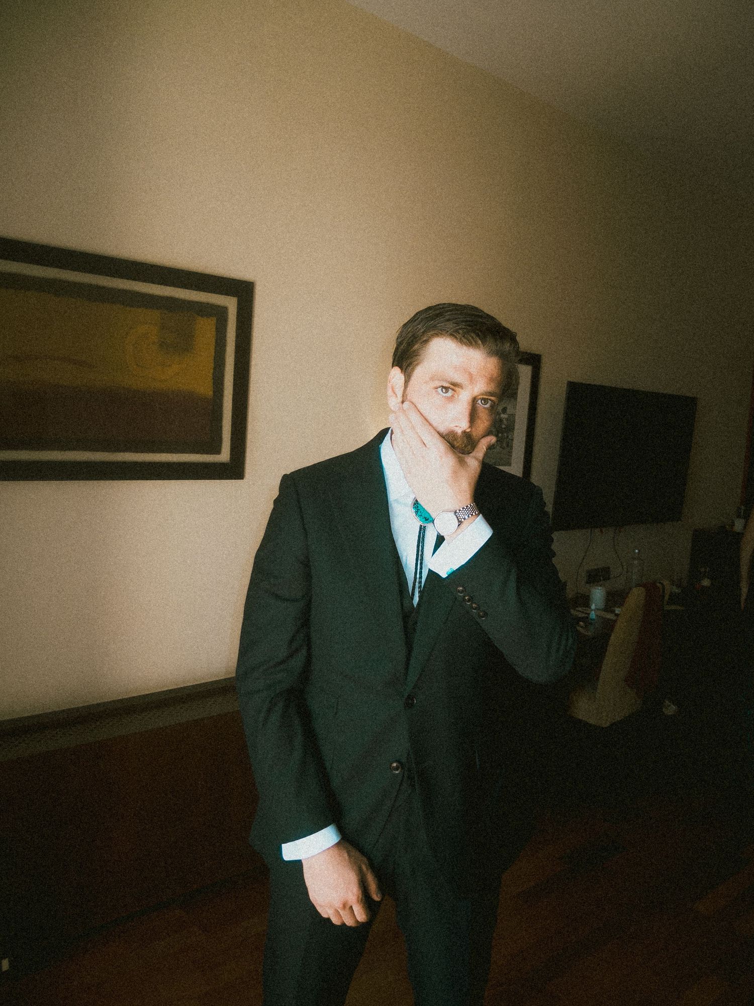 Sequence of groom in dark suit adjusting tie in dimly lit room.