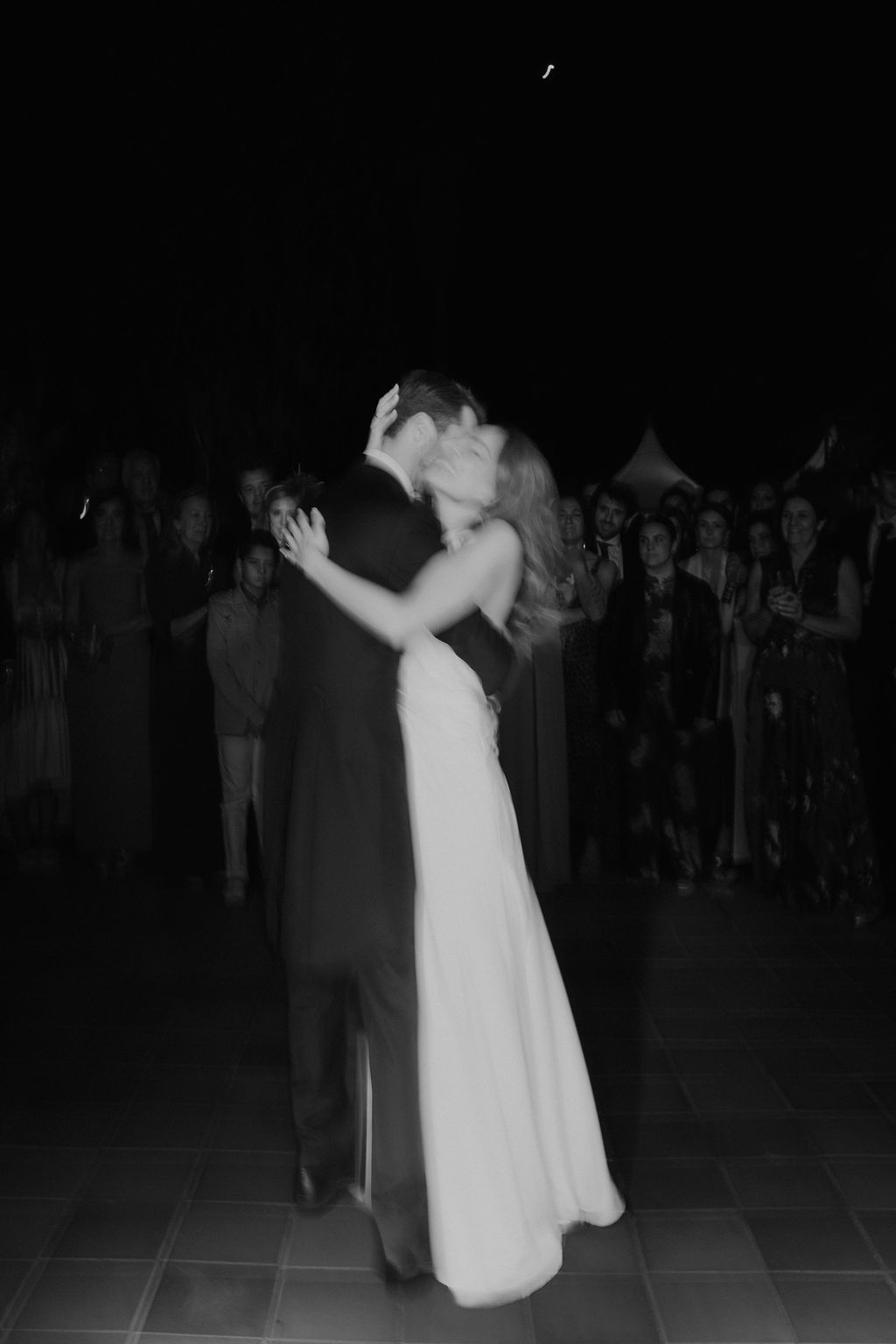 A couple shares their first dance at a wedding reception in a dimly lit venue.