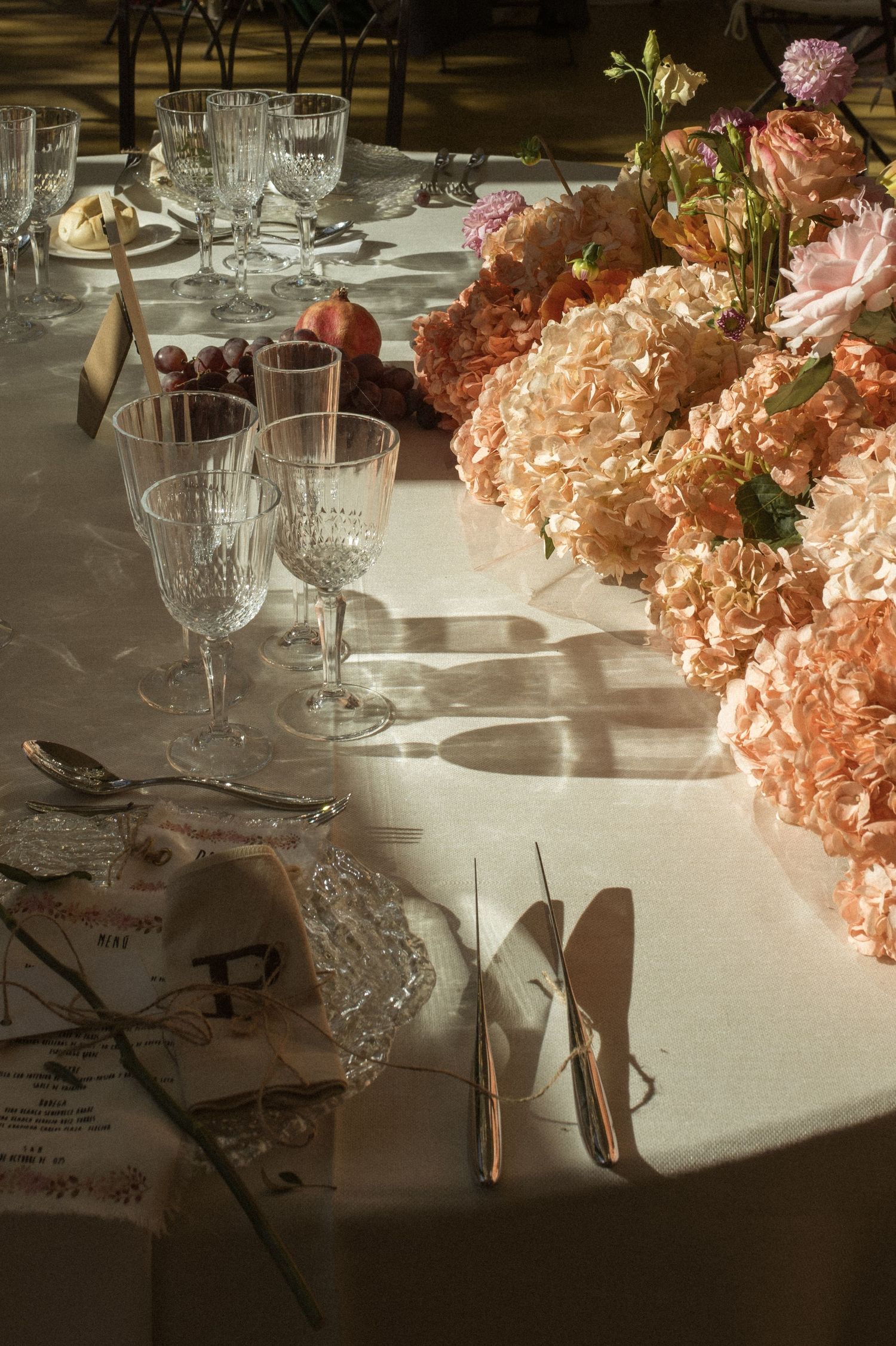Elegant table setting with crystal glasses and pink floral centerpieces in warm lighting.