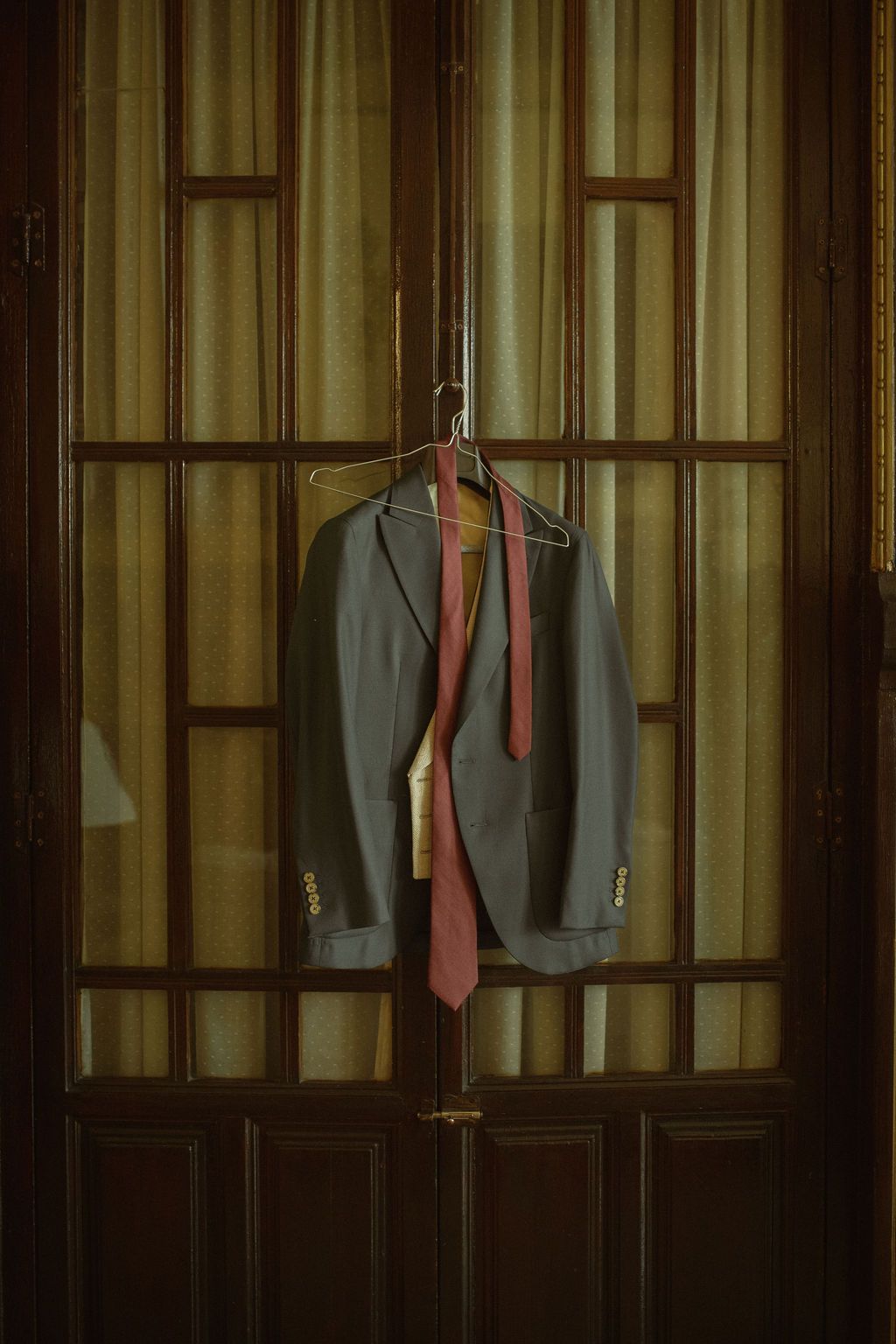 Formal suits and ties hanging on wooden wardrobe doors in warm lighting.