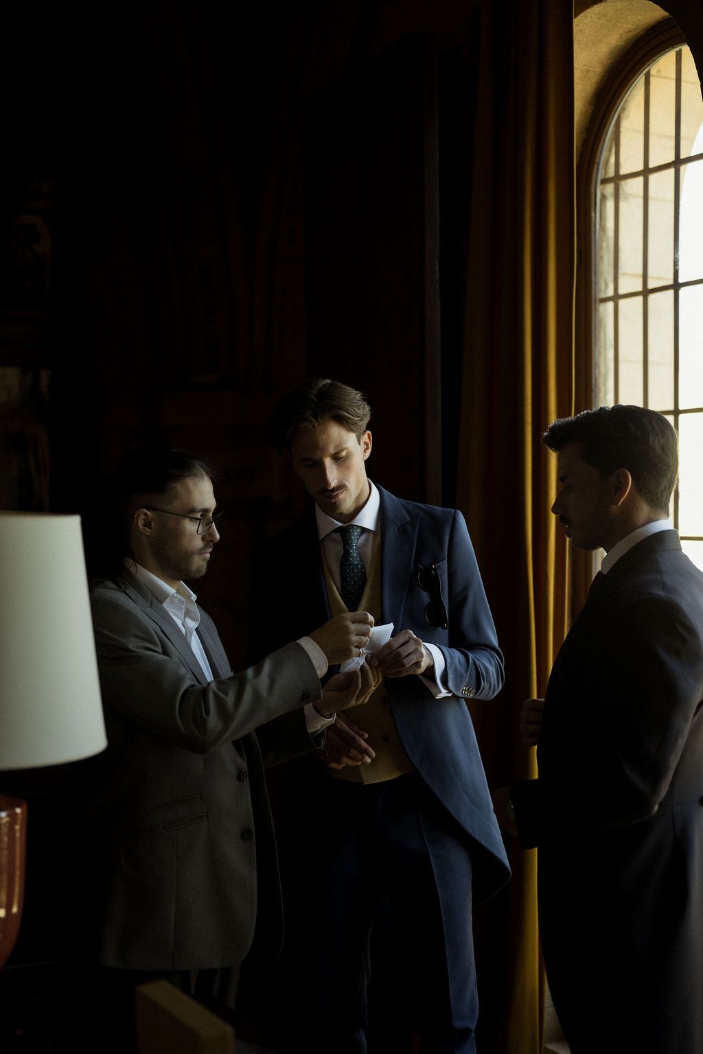 Two men in suits share an intimate conversation in a dimly lit room.