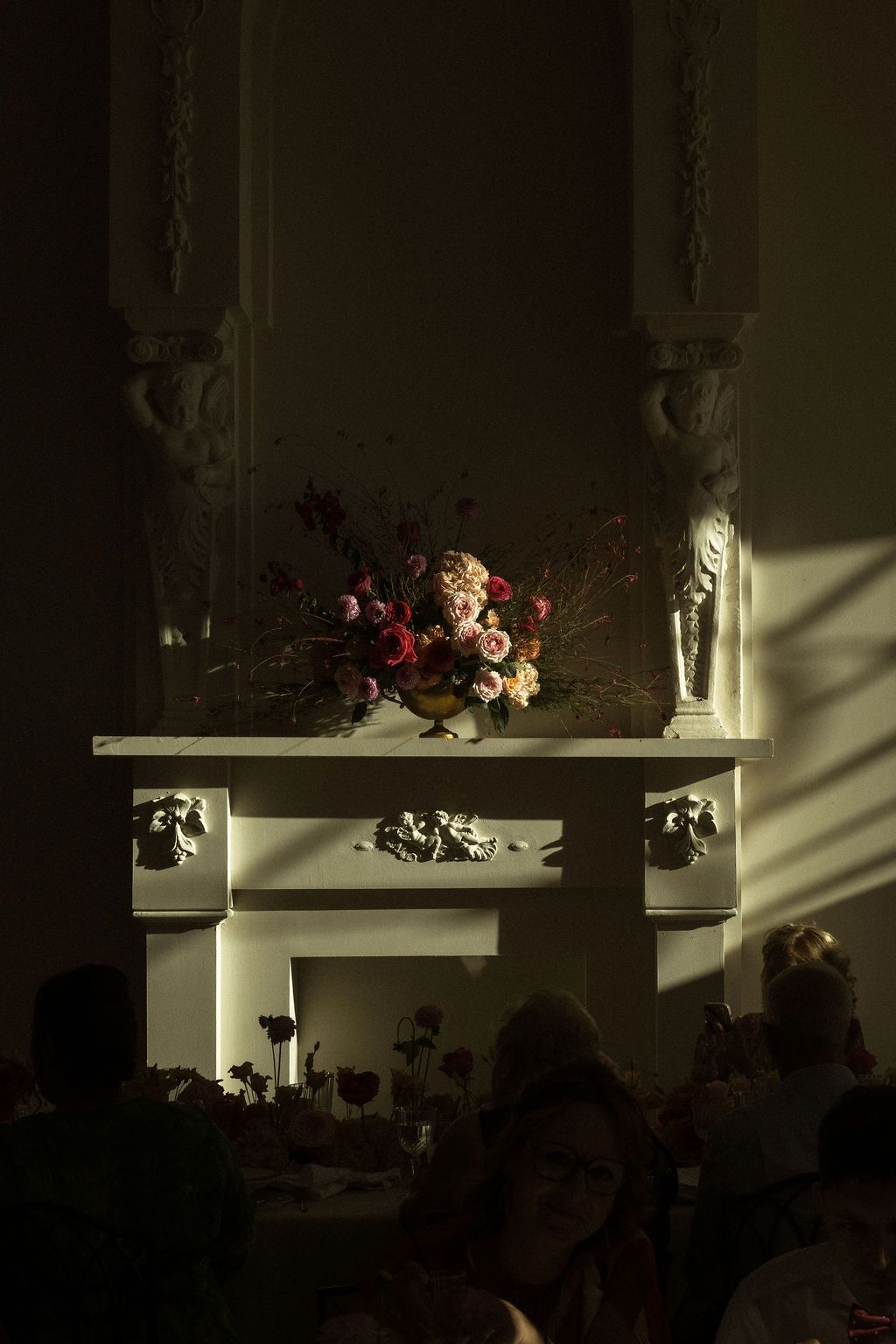 Dramatic shadows fall across white shelves decorated with floral arrangements.