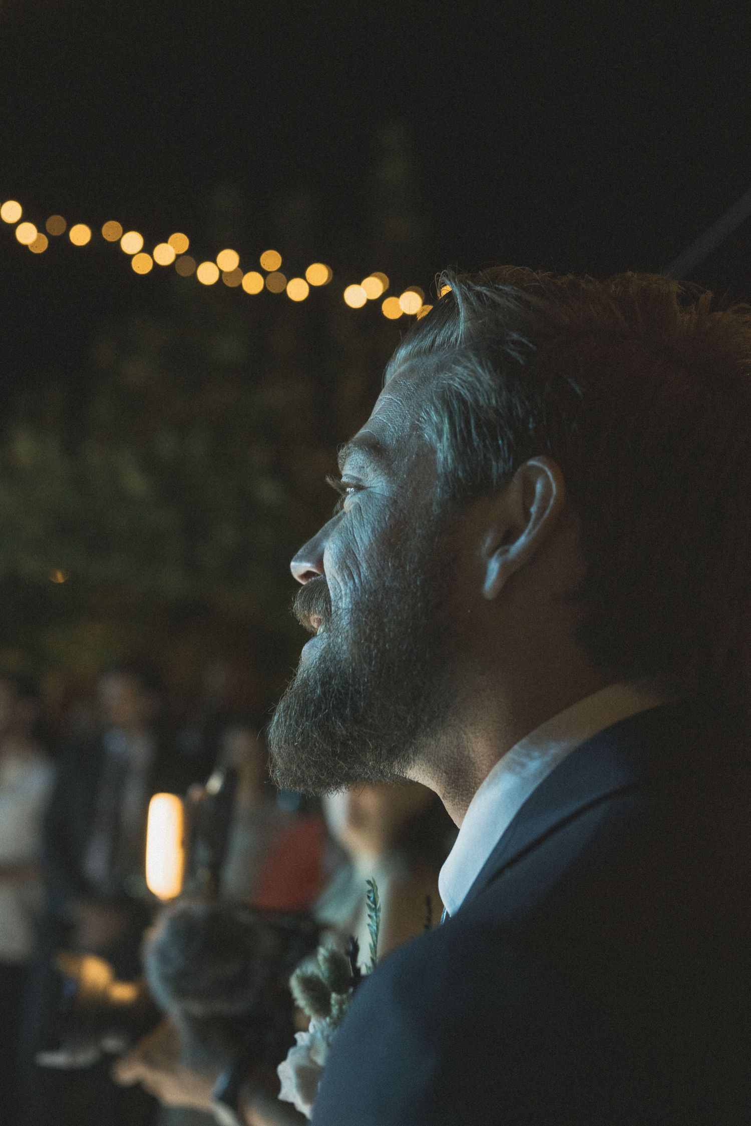 Evening reception guests illuminated by warm string lights overhead.
