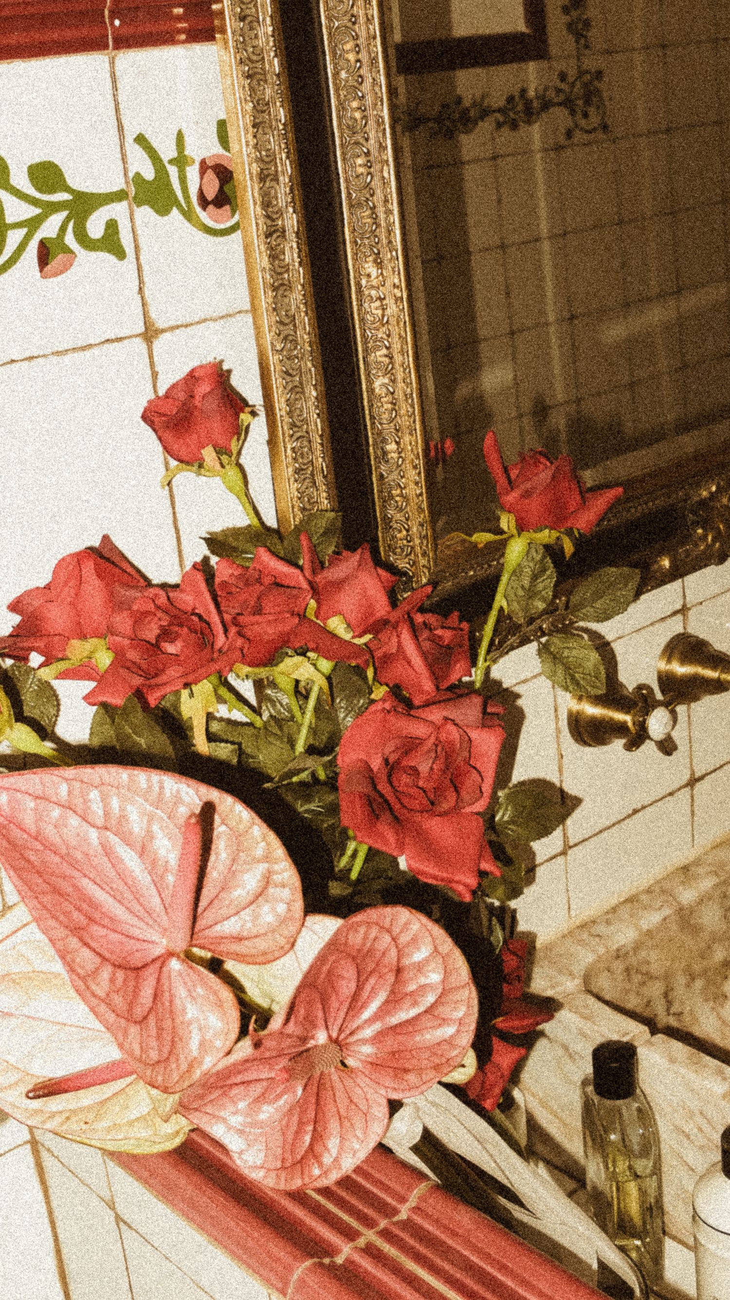 Red roses and pink anthurium flowers arranged near an ornate gold-framed mirror.