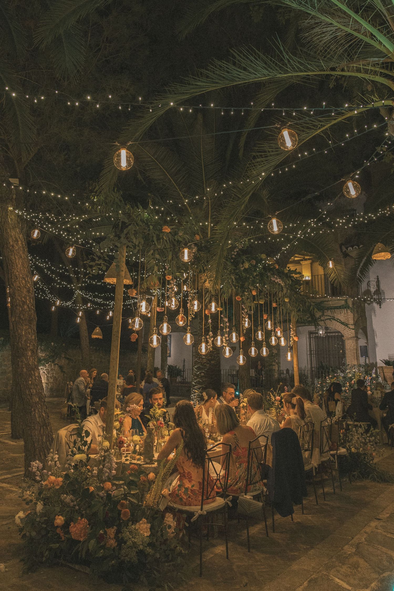 Outdoor wedding reception under trees with string lights creating a magical ambiance.