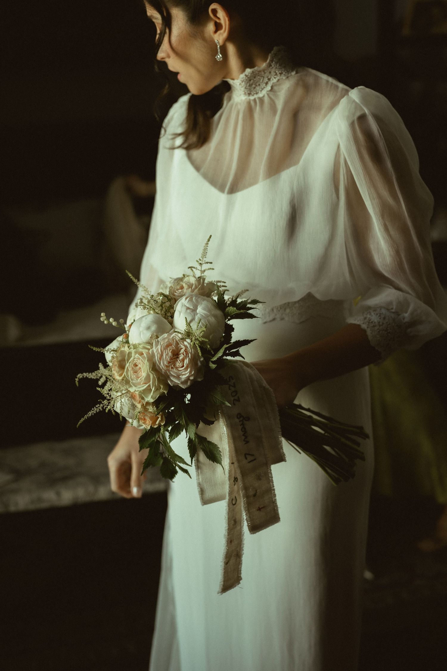 Classic white wedding dress with delicate floral details and sheer sleeves in dramatic lighting.