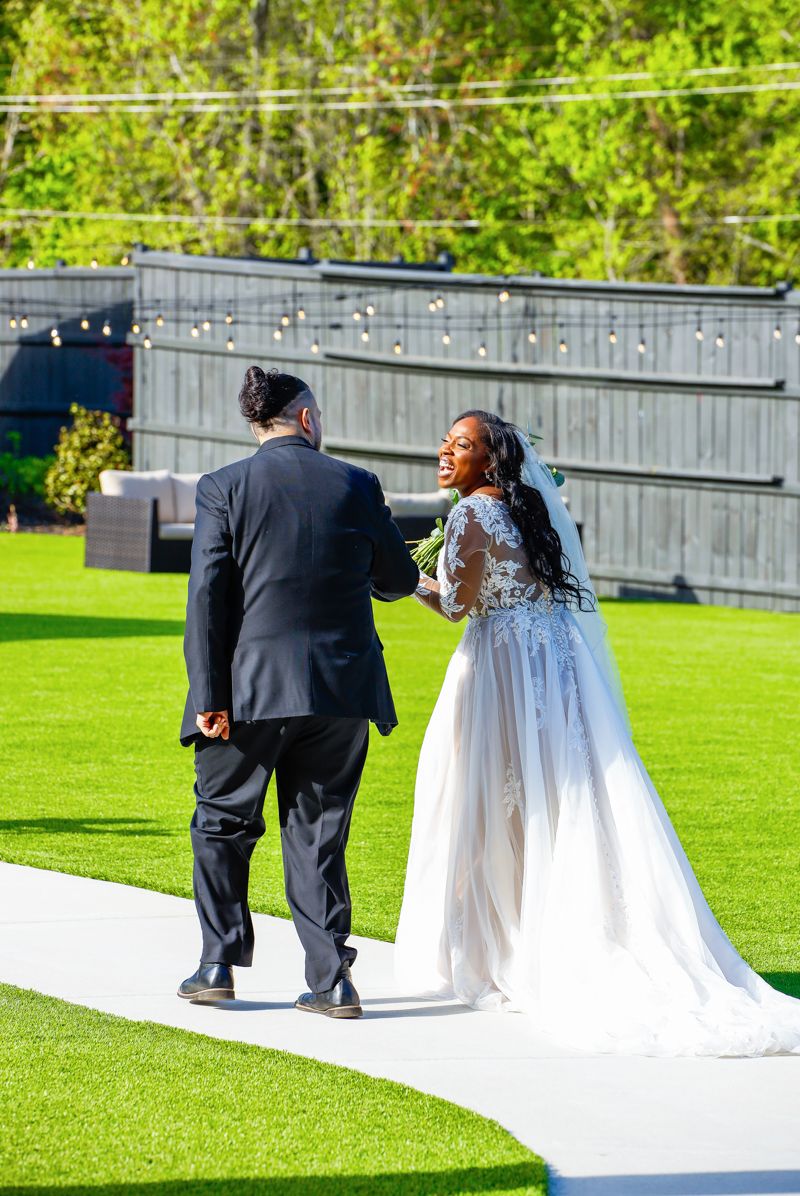 A couple walking on a lush green lawn during their wedding day, with the bride wearing a flowing white gown with lace details.