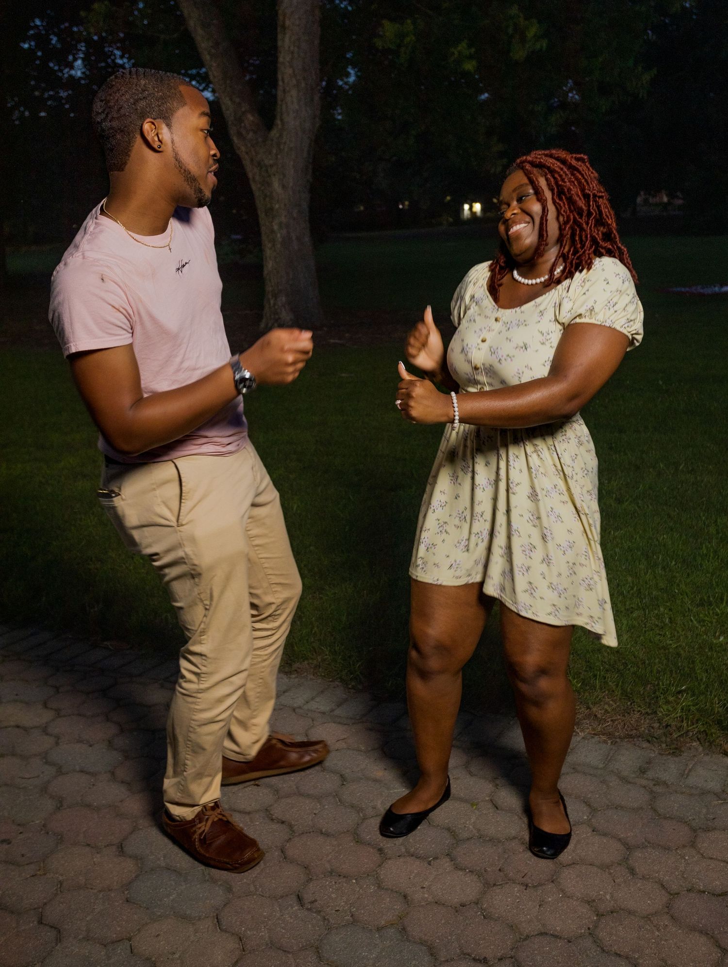 A couple dances together in a park setting on a paved pathway at dusk.