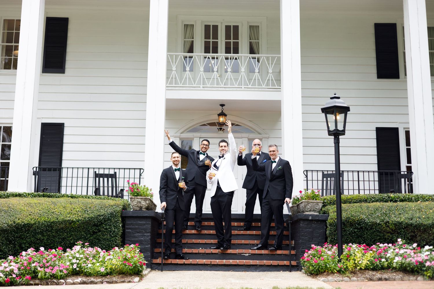 Wedding party posed on the steps of a classic white colonial style mansion.