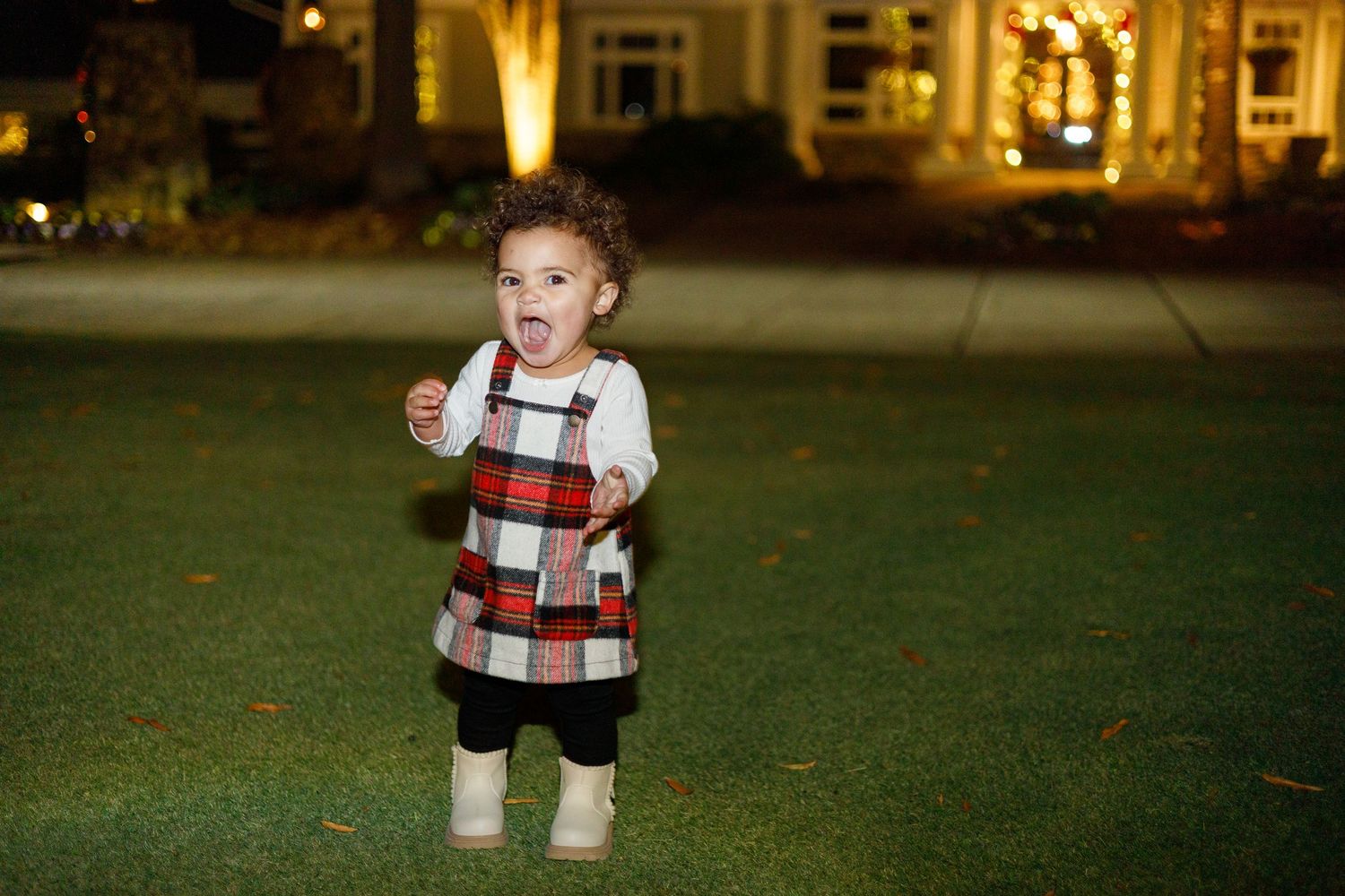 Small child wearing a patterned sweater plays on a grassy lawn at dusk.
