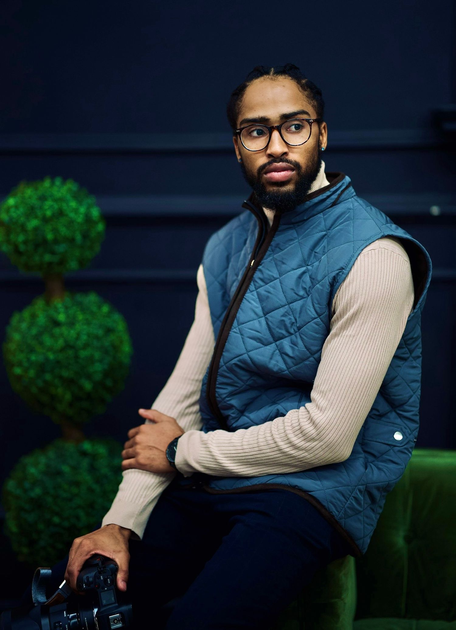 Portrait session in navy quilted vest and cream sweater against dark background.