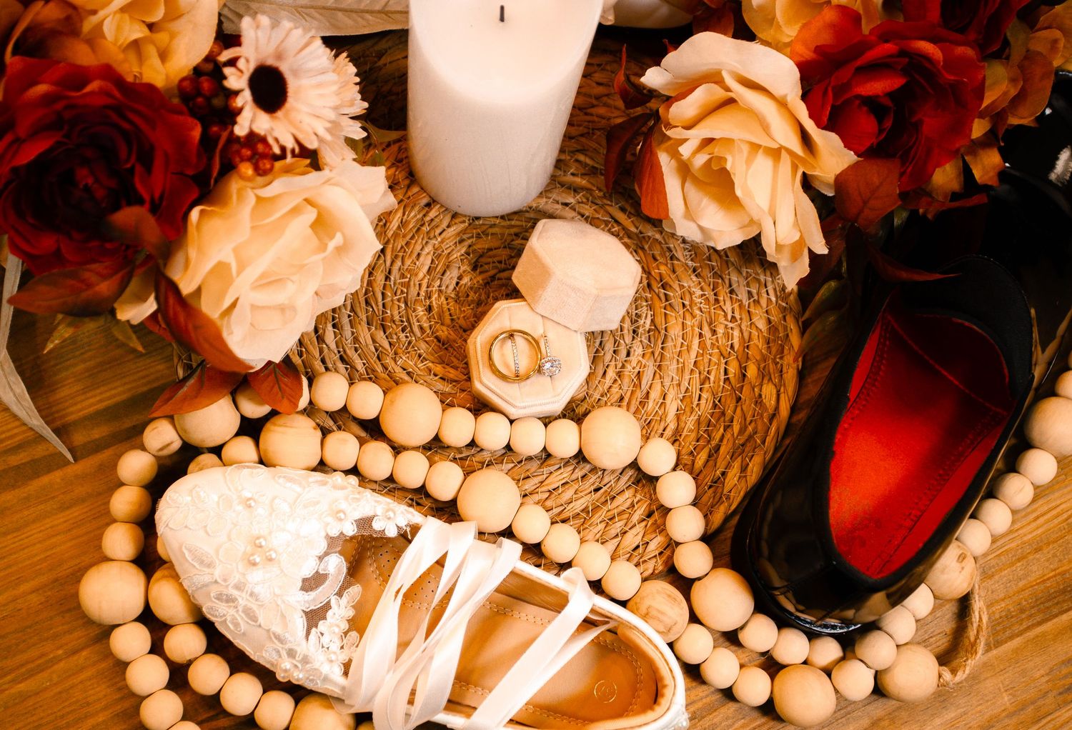 Wedding details featuring roses, candles, and decorative wooden beads arranged on a textured surface.