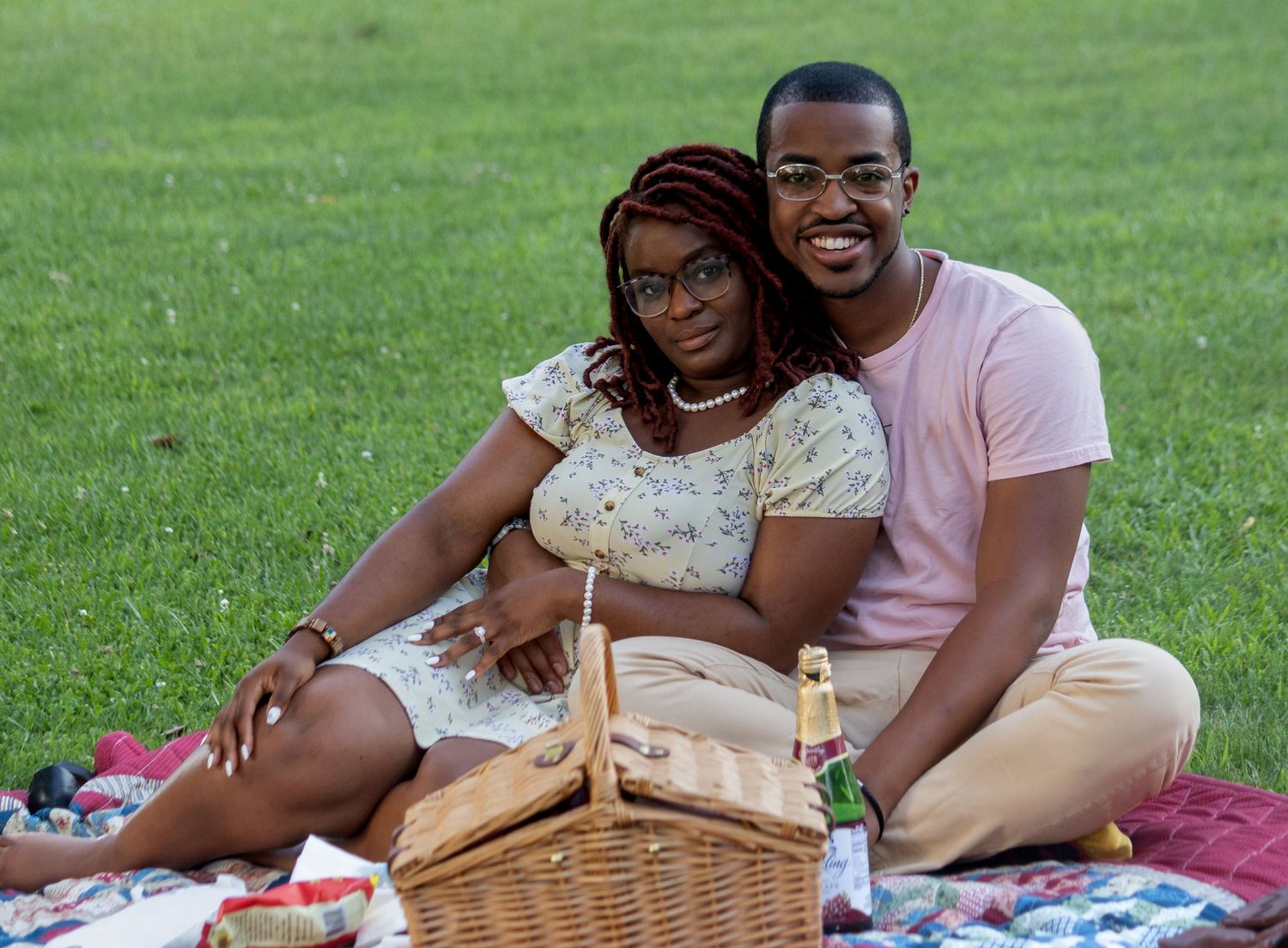 People enjoy a romantic picnic on a grassy lawn with a wicker basket and blanket on a sunny day.