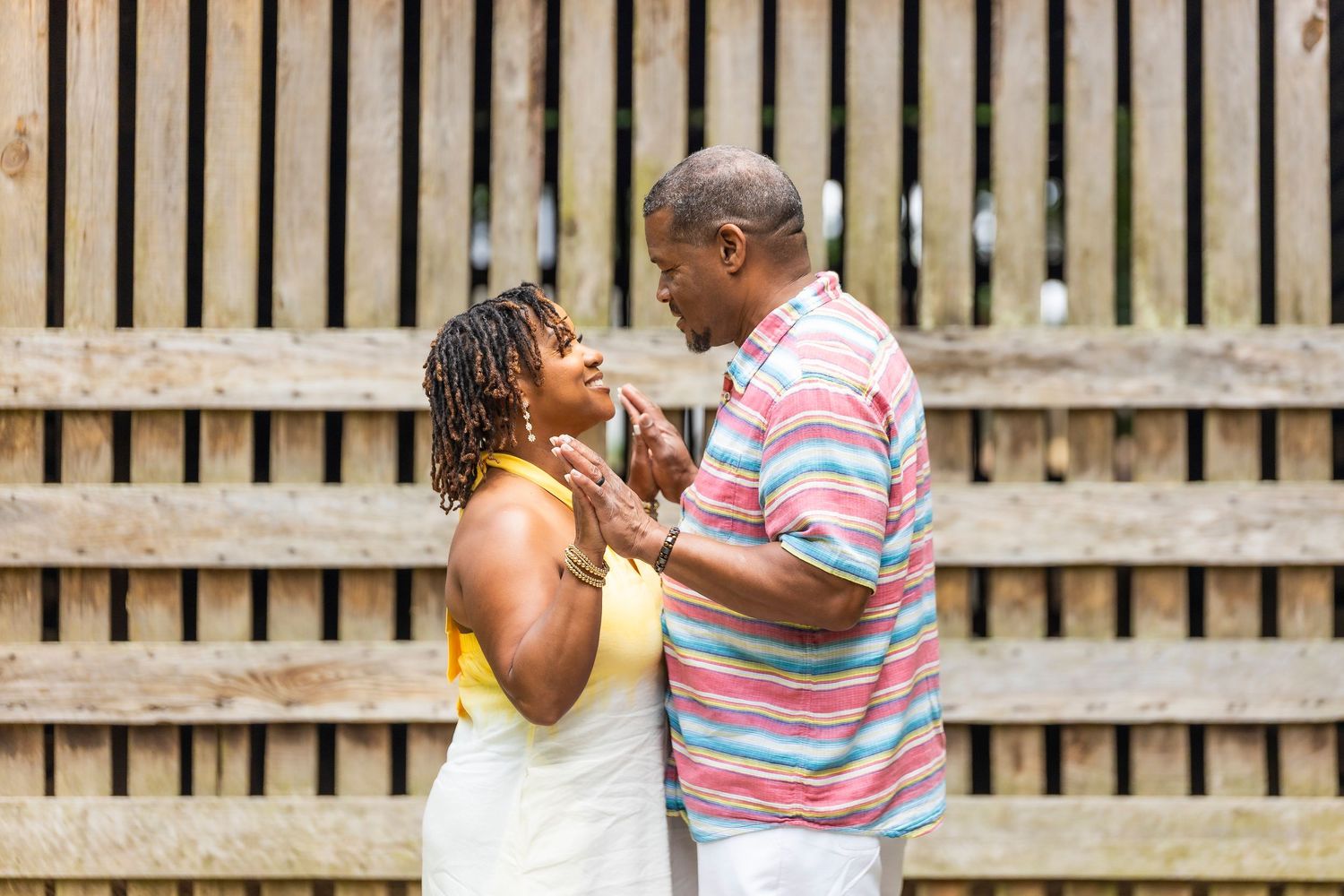 A couple dances together on a wooden deck surrounded by a picket fence during an outdoor celebration.