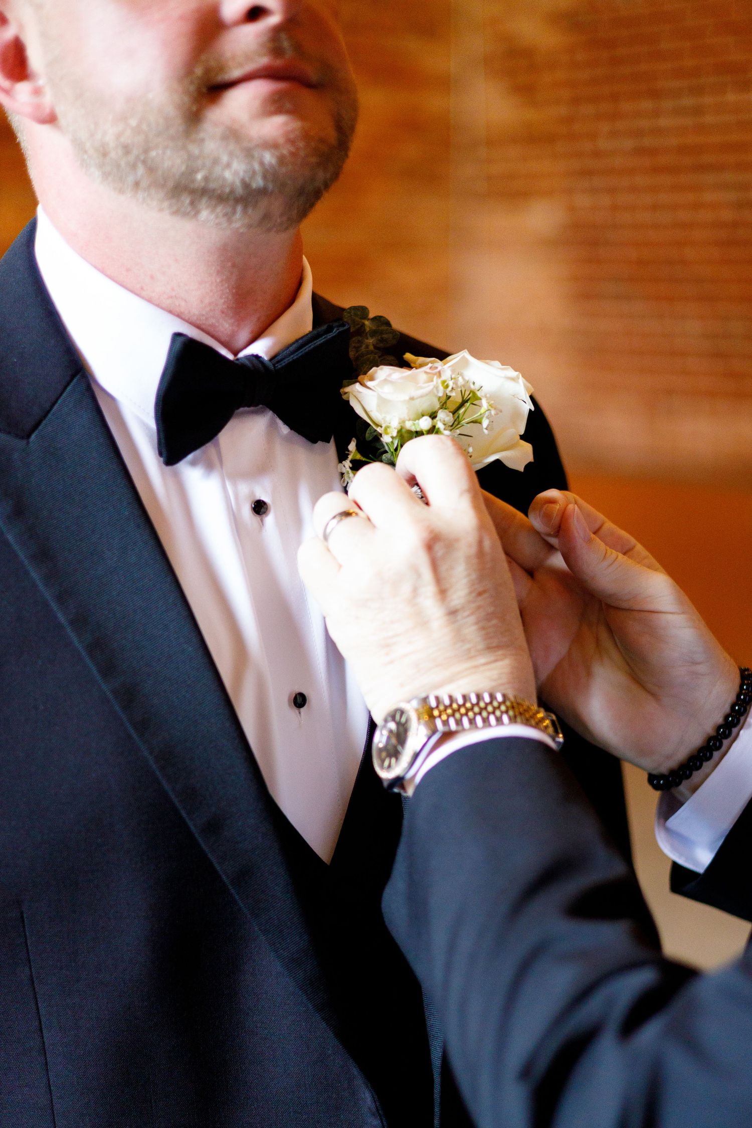 A close-up shot of a formal black tuxedo with white boutonniere being pinned on the lapel.