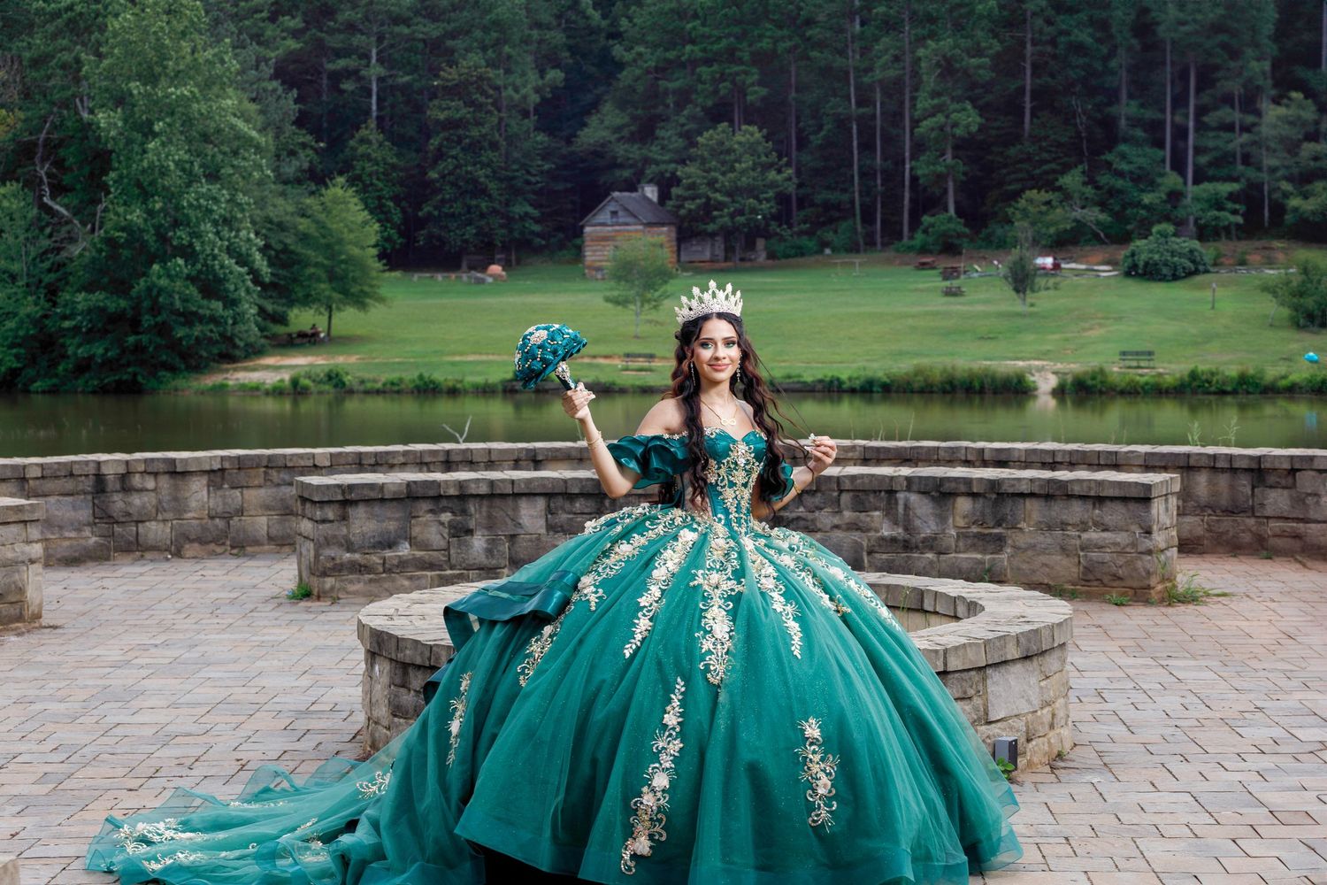 A stunning emerald green ball gown with gold embroidery photographed in a stone courtyard setting.