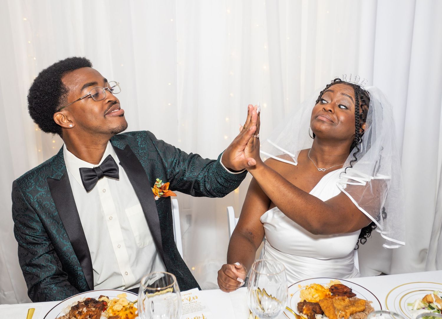 A couple shares a playful high-five moment during their wedding reception.