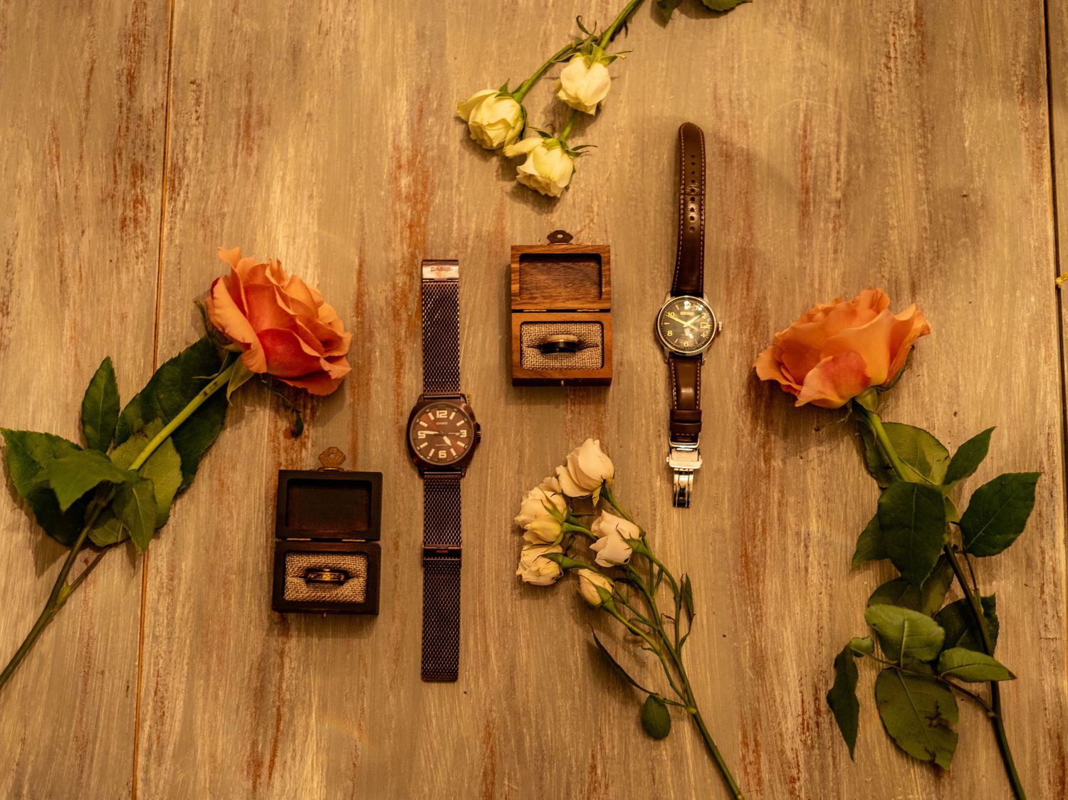 Vintage watches and rings arranged with orange and yellow roses on wooden background.