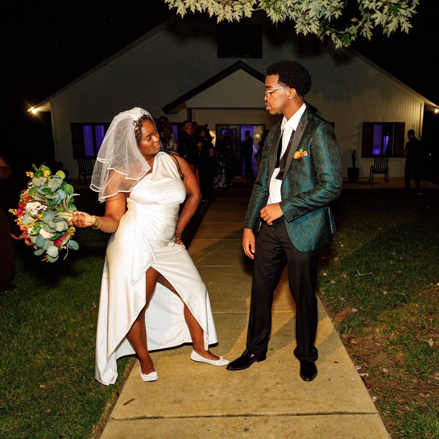 A couple shows off their dance moves on their wedding day outside a venue at night.