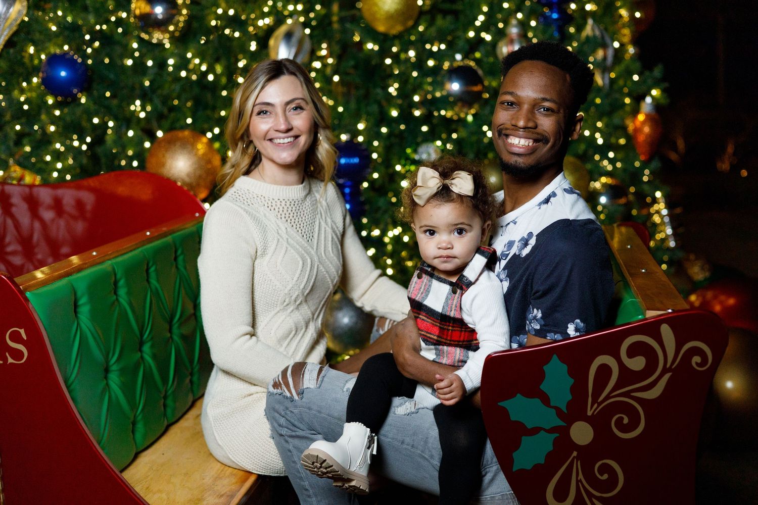 Family poses together for holiday portraits in front of a decorated Christmas tree with twinkling lights and ornaments.