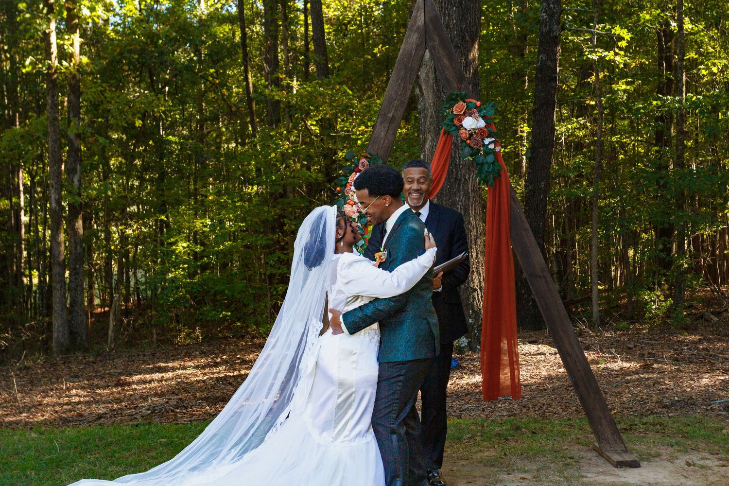 Wedding party poses for photos in a scenic wooded outdoor setting with beautiful natural lighting.