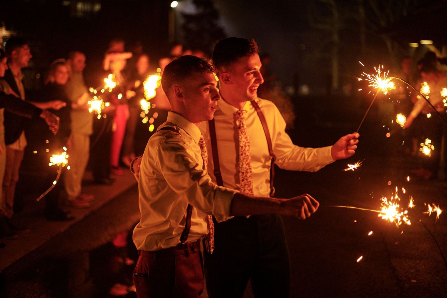 Wedding guests hold sparklers creating a magical nighttime celebration atmosphere at an outdoor reception.