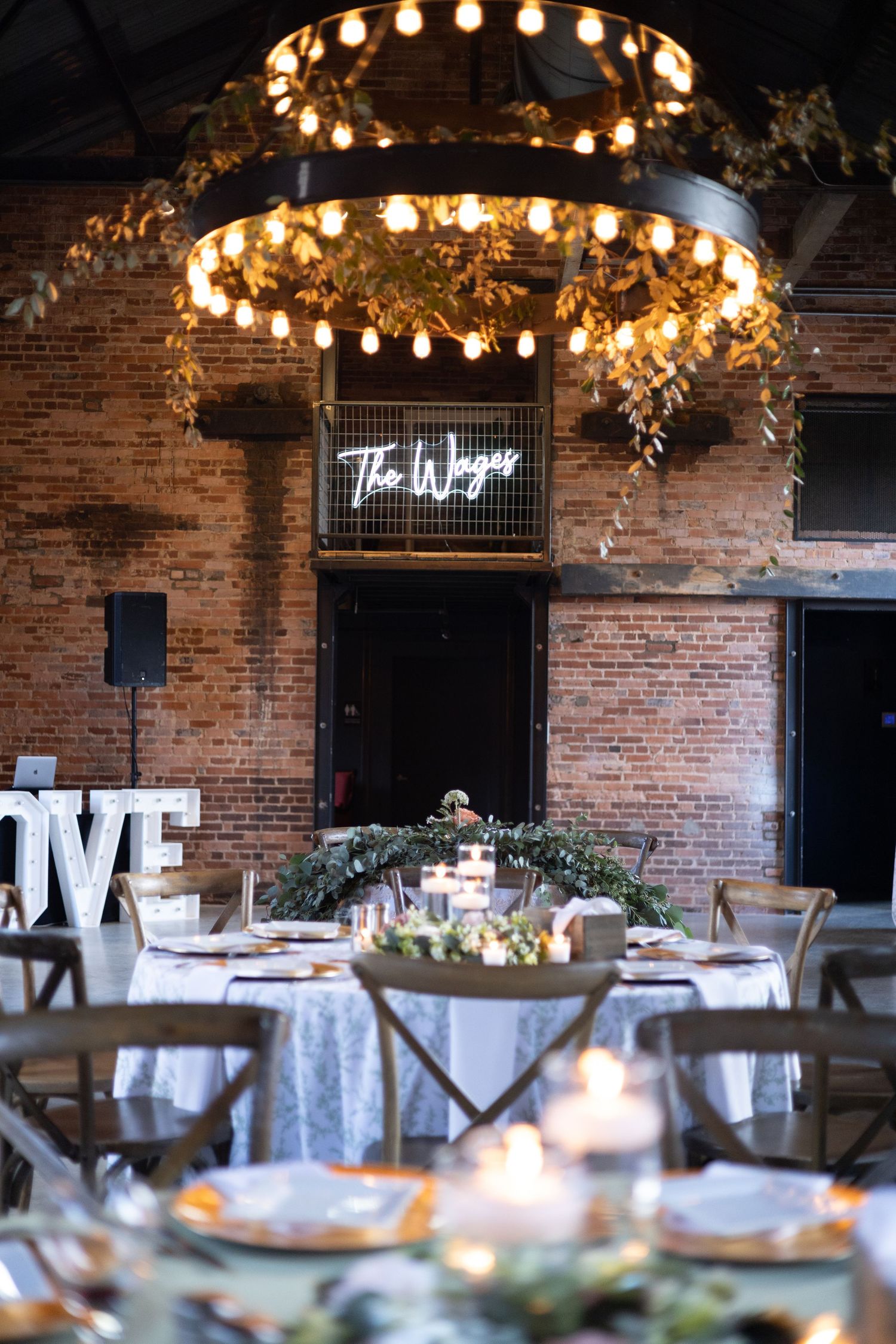 Rustic wedding reception venue with exposed brick walls, circular chandeliers, and elegant table settings.