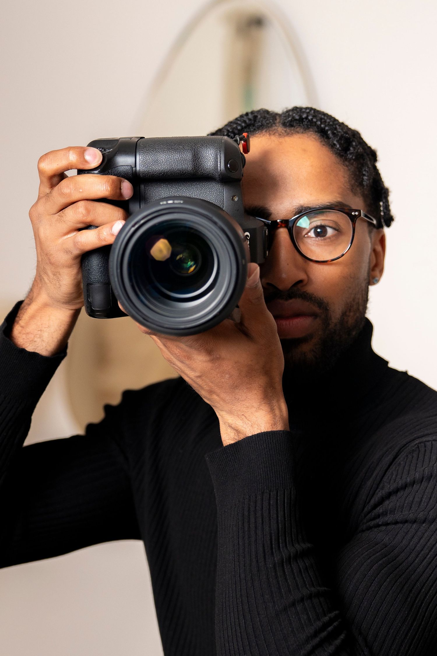 A photographer wearing glasses and a black sweater holding a professional camera.