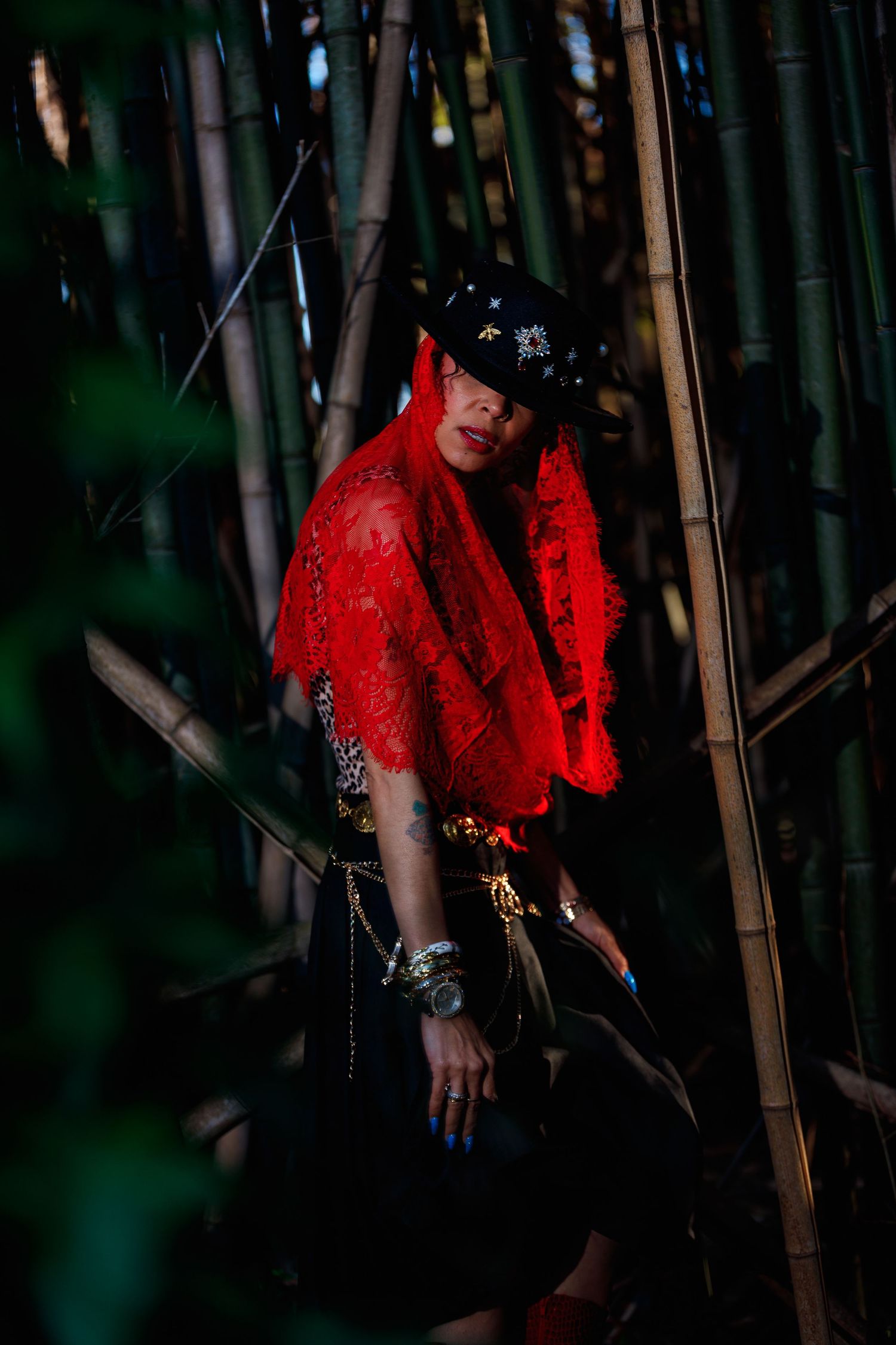 Person in a vibrant red dress poses dramatically against bamboo stalks in a dark forest setting.