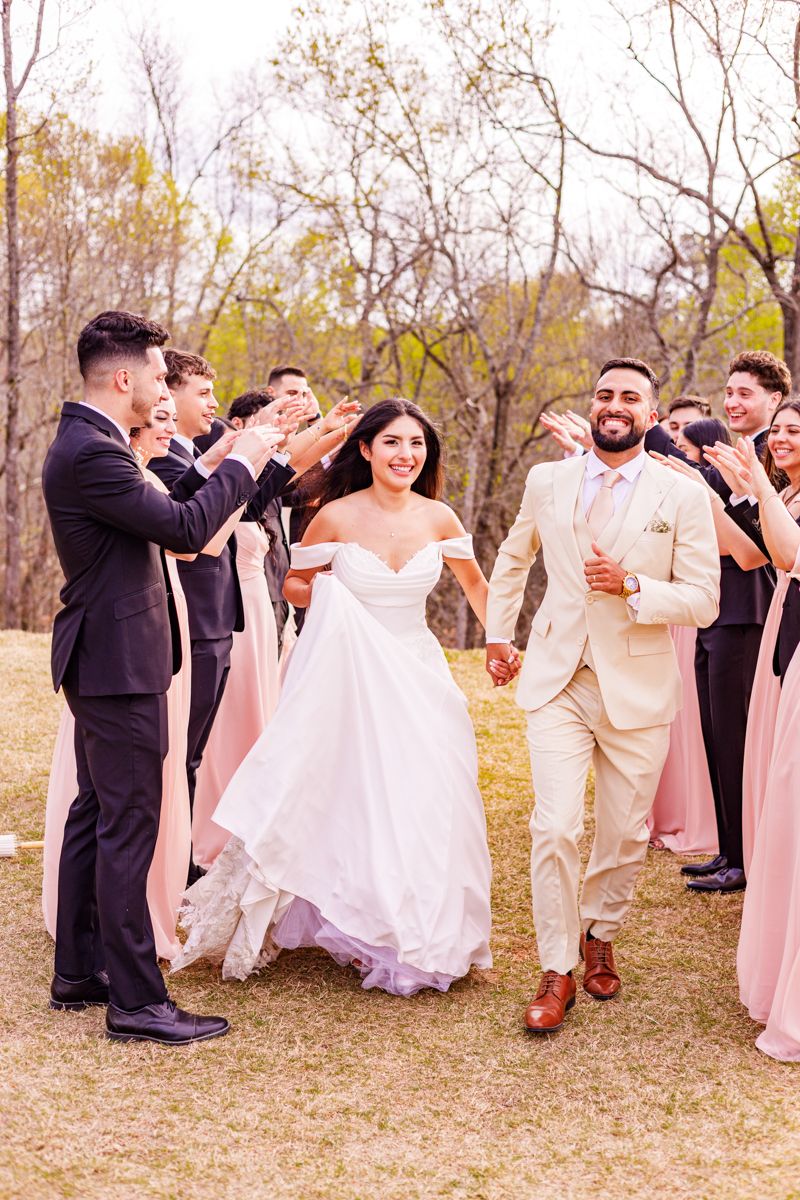 Wedding party in black and beige attire posing together on grassy outdoor grounds.